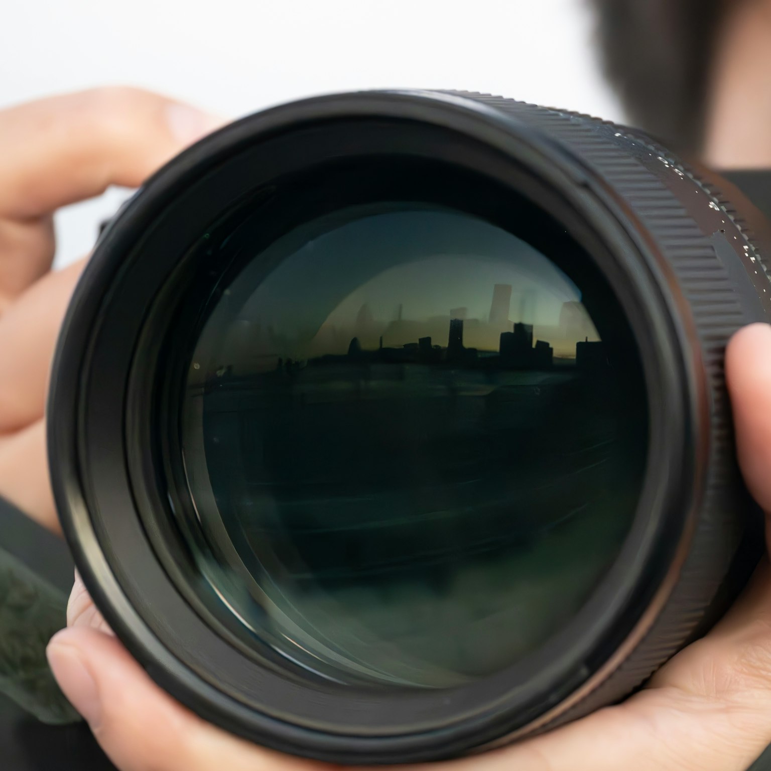 Person holding a camera lens with a cityscape reflection