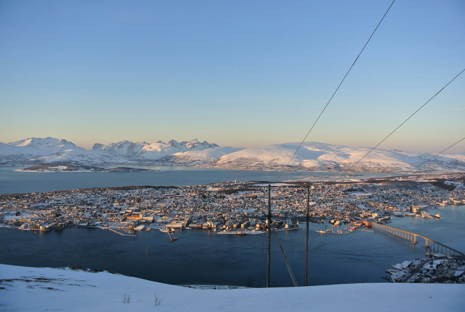 Eine malerische Aussicht auf die Stadt Tromsø, die mit Schnee bedeckt ist, mit umliegenden Bergen
