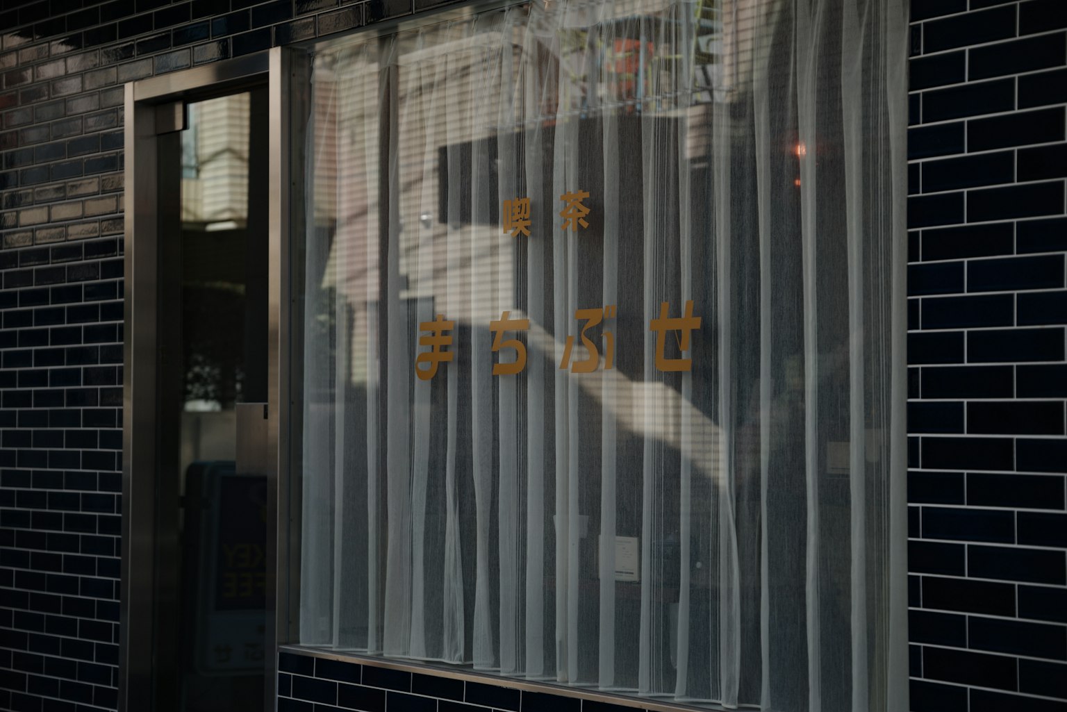 A window with white curtains and golden text on a black tiled wall