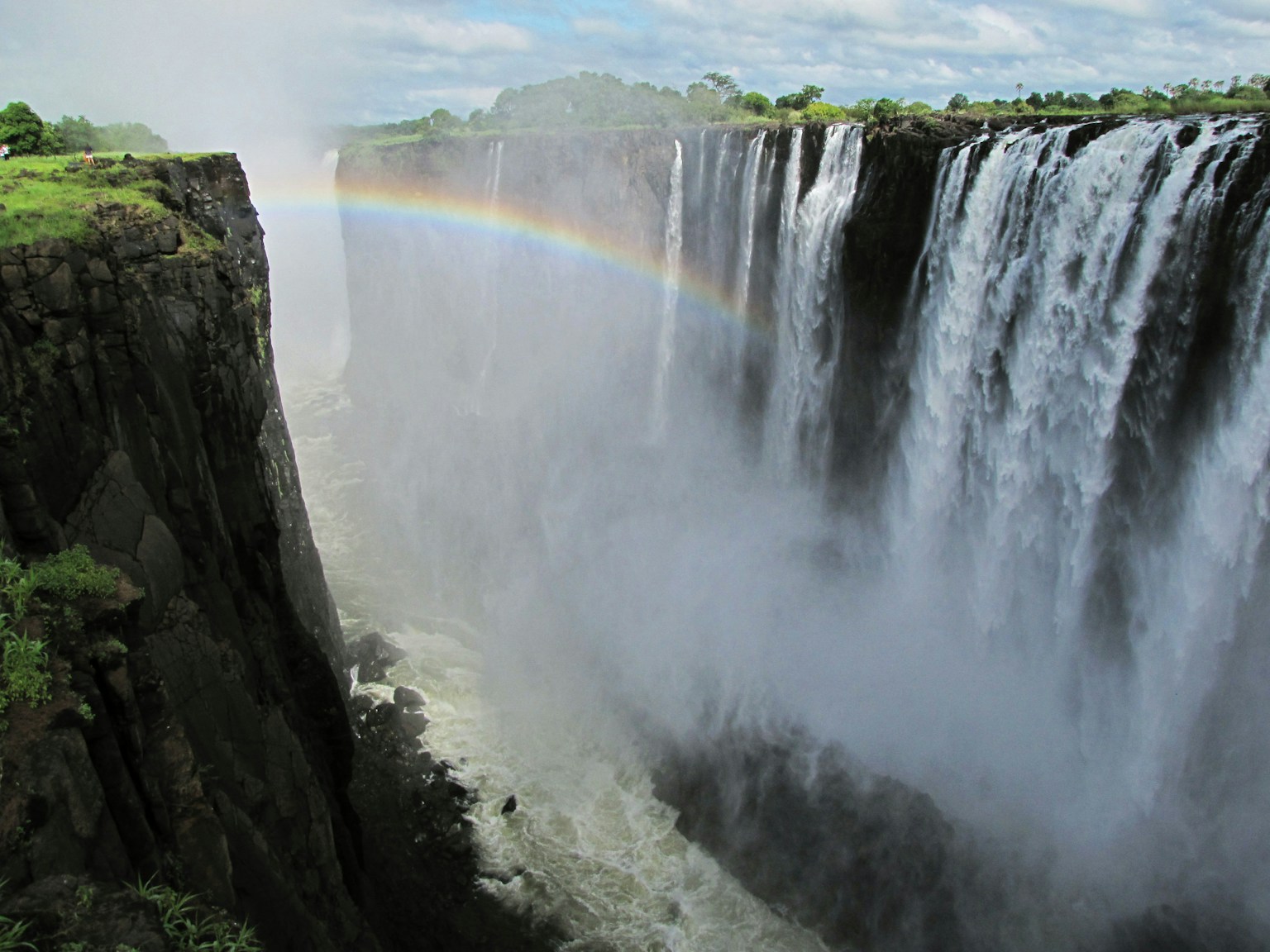 Vista maestosa delle Cascate Vittoria con nebbia e un arcobaleno