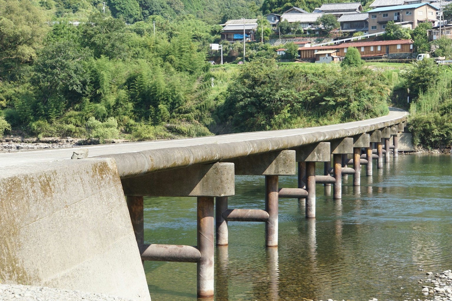 Ponte in cemento che attraversa un fiume con un villaggio sullo sfondo