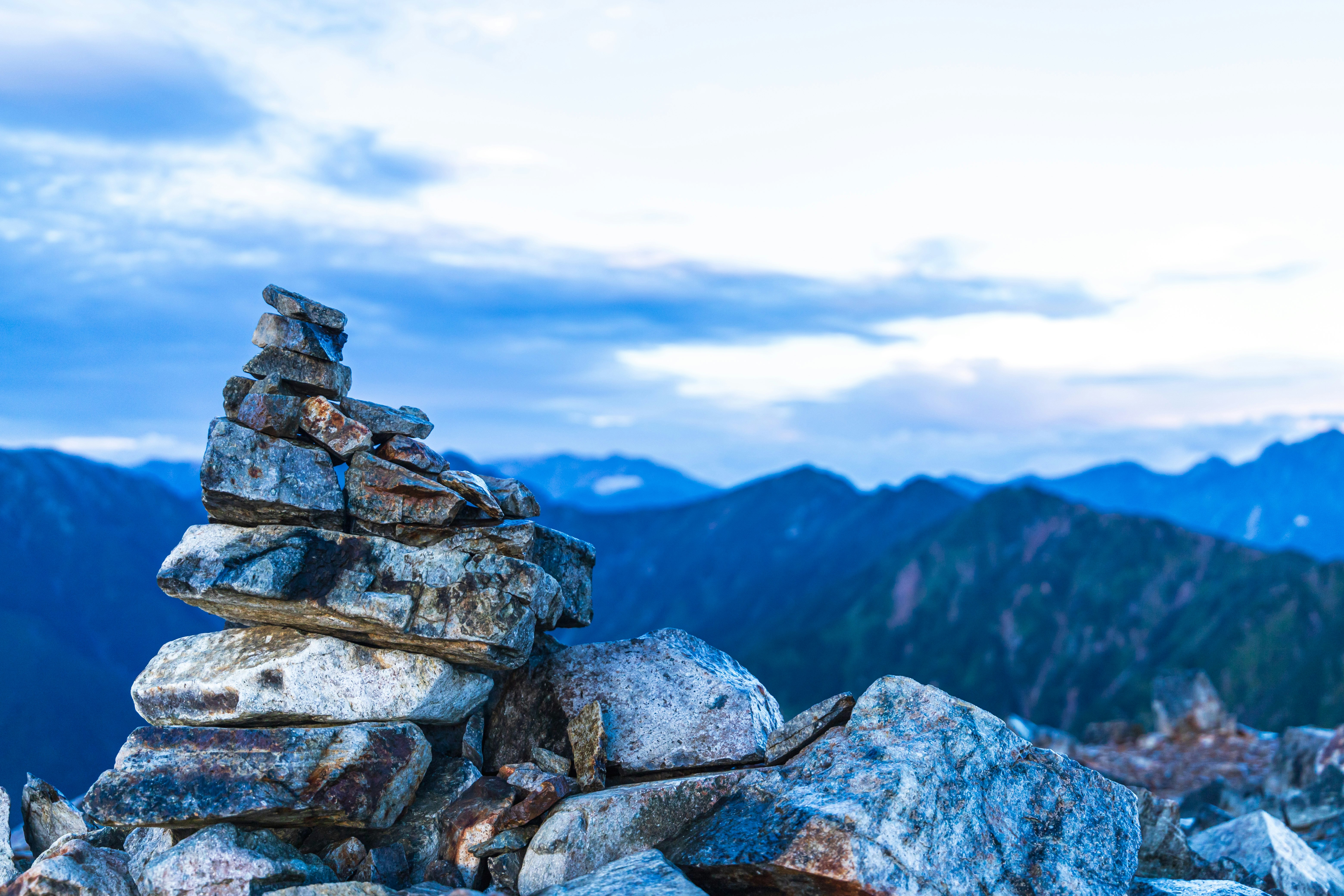 đống đá (cairn) trên đỉnh núi với cảnh sườn núi màu xanh