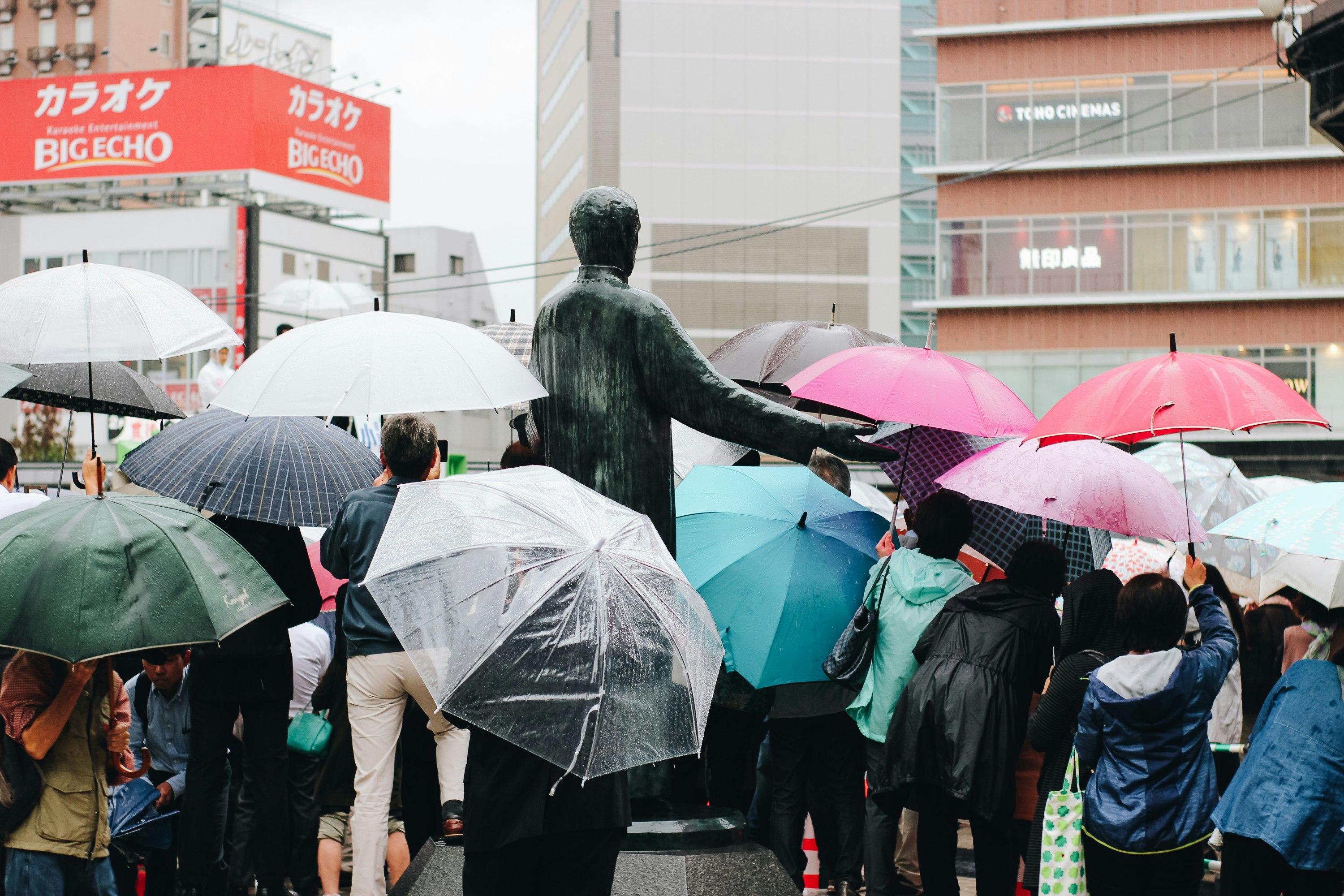 雨の中で傘をさす人々が並ぶ街角