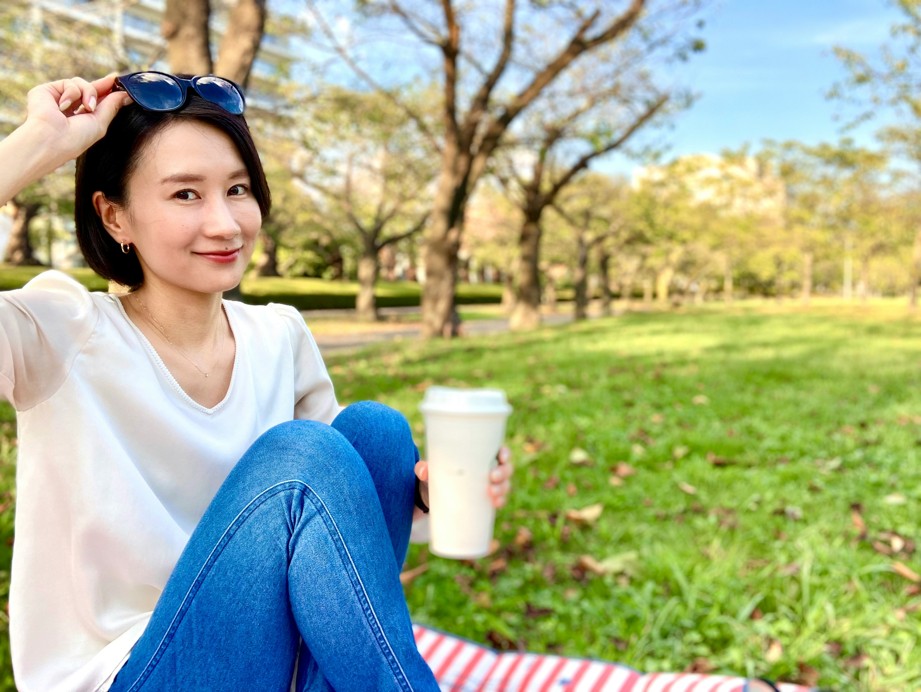 공원에서 파란 청바지를 입은 여성이 음료를 들고 앉아 있는 모습