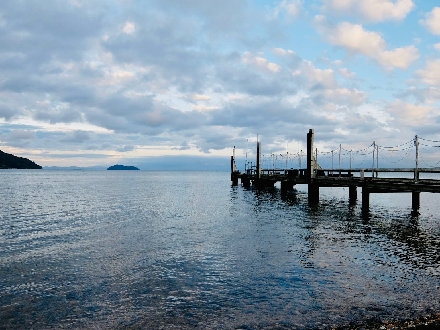 Calm sea with a cloudy sky featuring a wooden pier