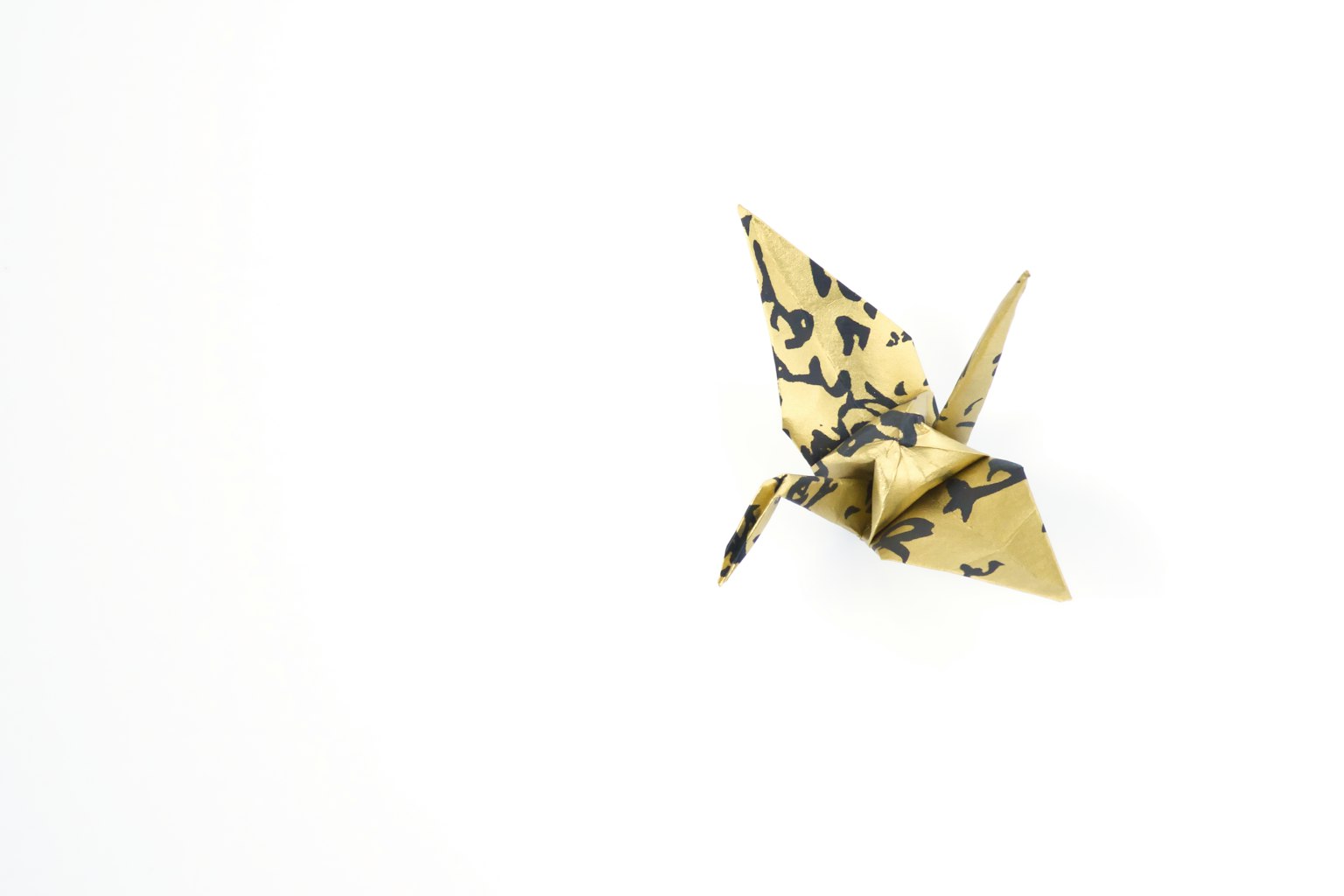 Seekor burung bangau origami emas mengapung di latar belakang putih