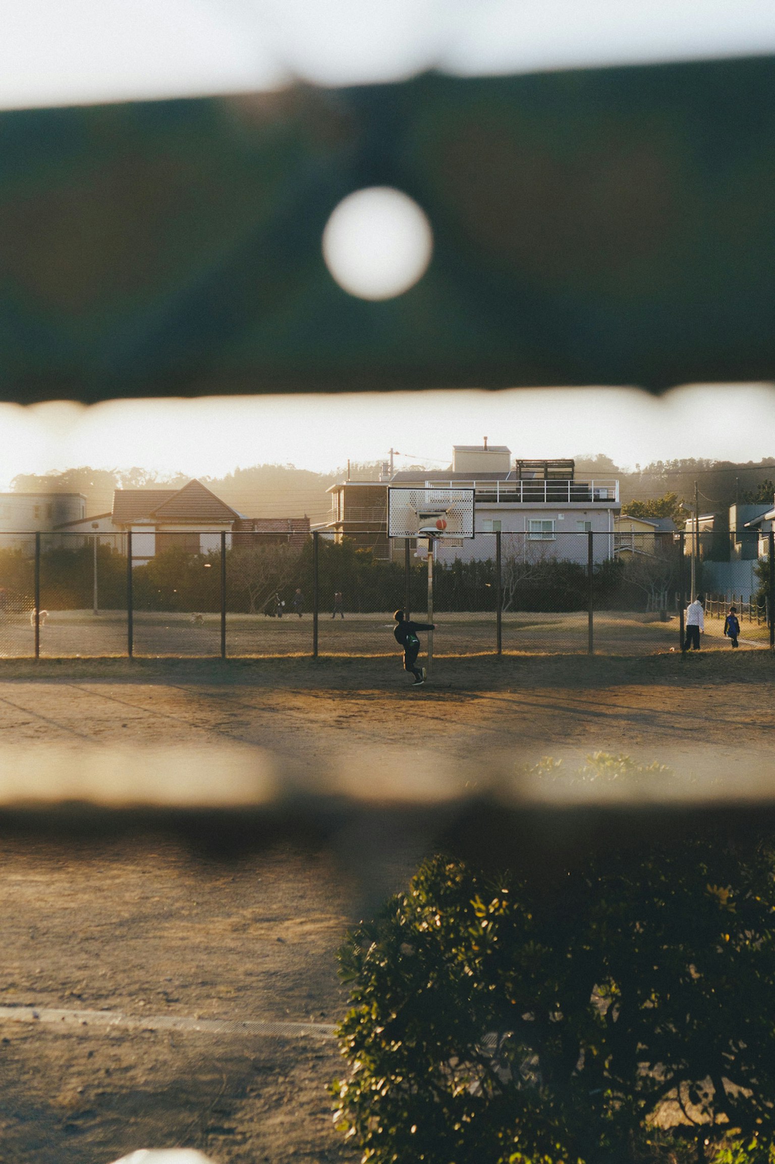 Blick auf einen Tennisplatz und umliegende Gebäude durch einen Zaun