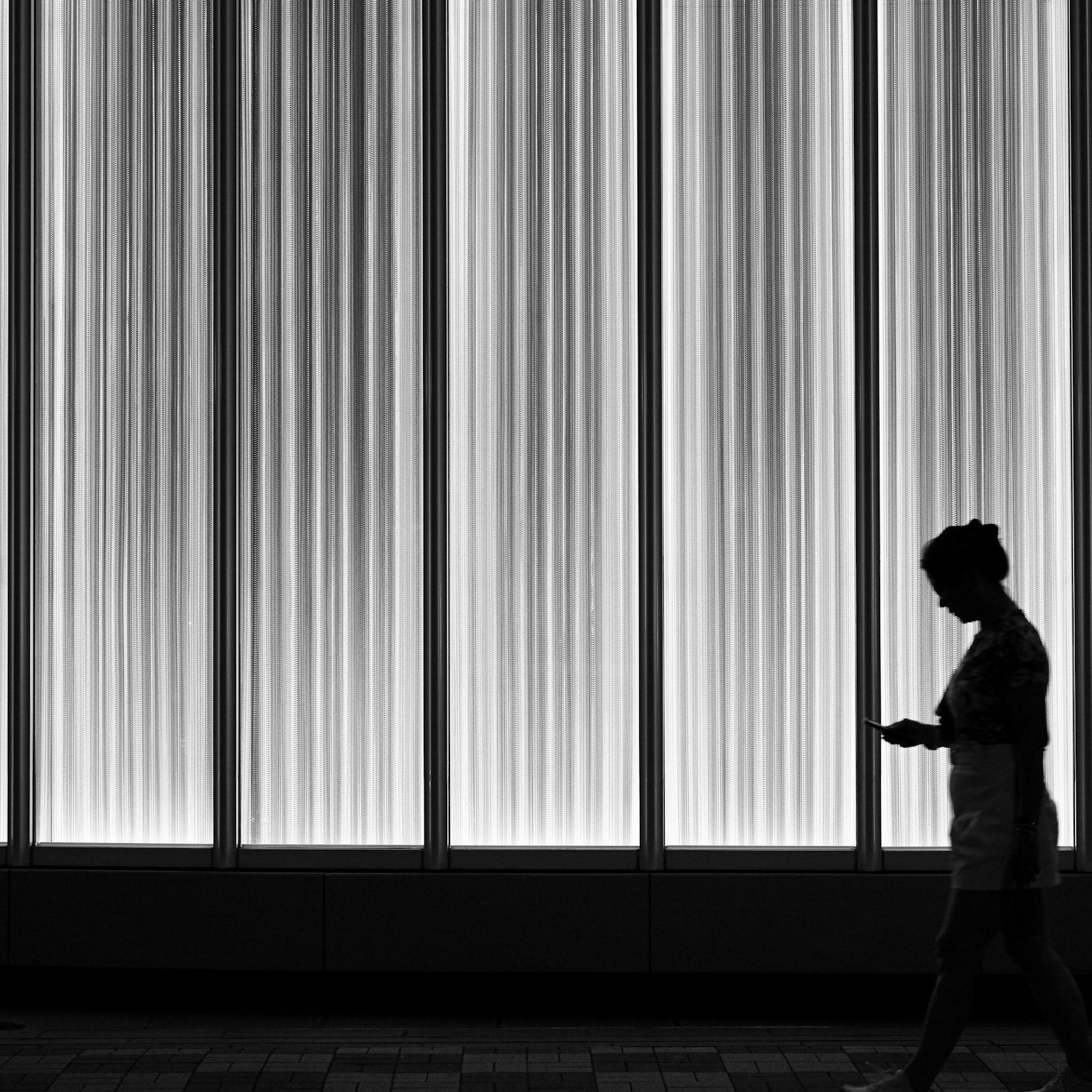 白黒の背景にシルエットの人物がスマートフォンを持って歩いている