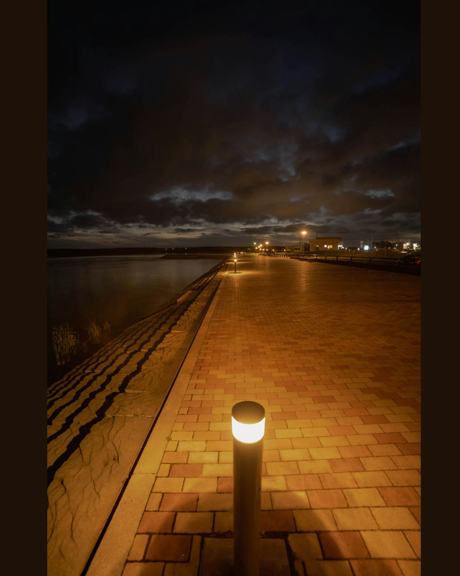 Paseo costero de noche con un farol y cielo nublado