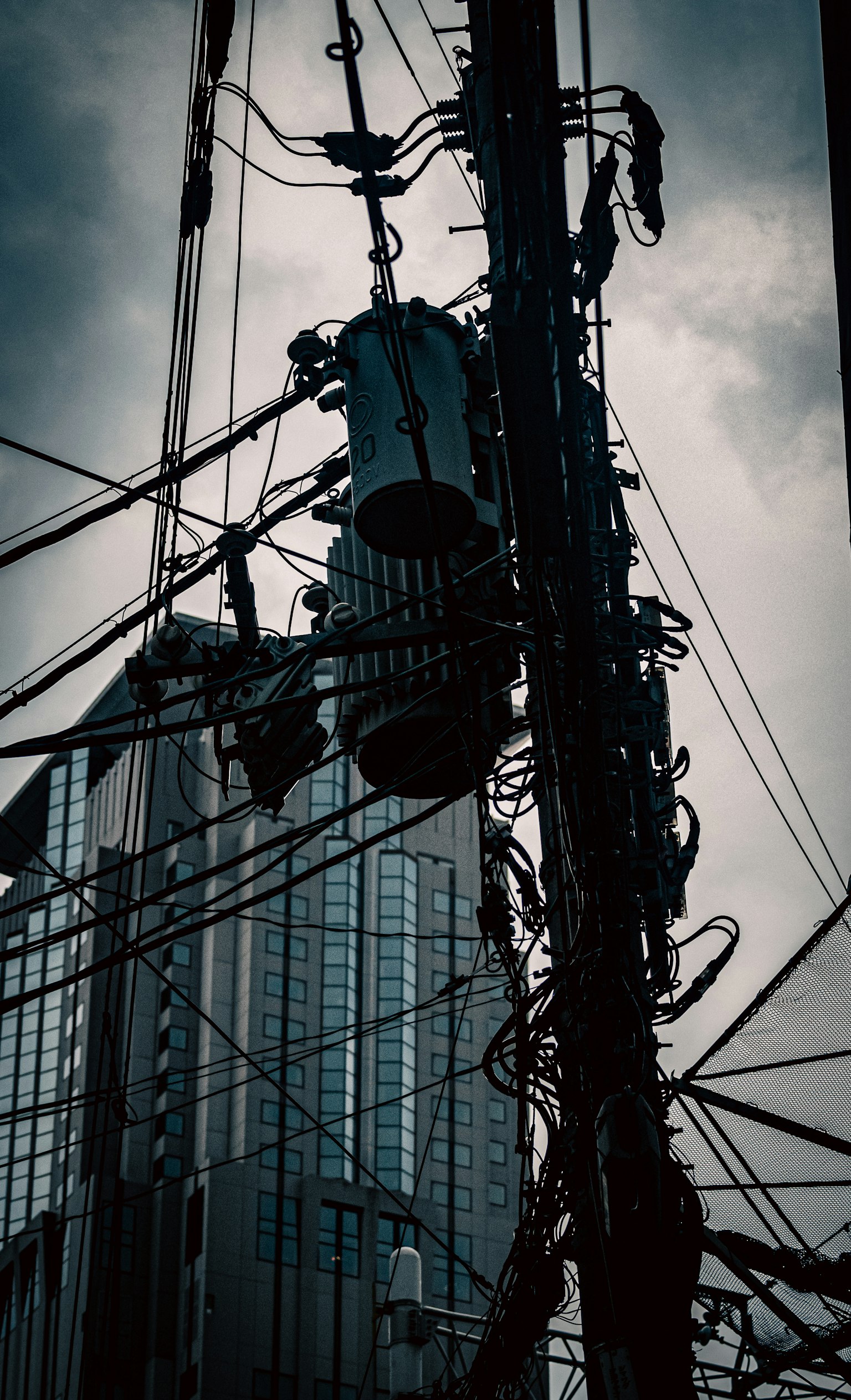 Imagen en primer plano de líneas eléctricas y un poste detrás de un edificio