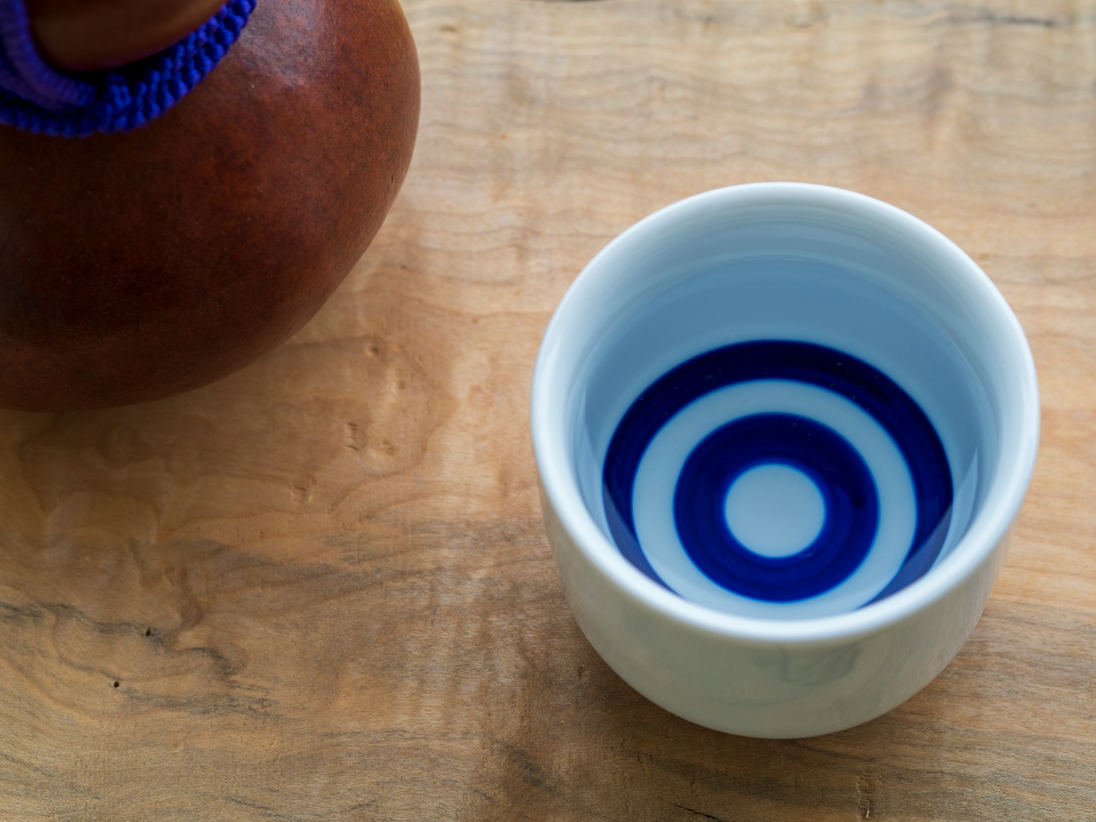 Una ciotola di ceramica bianca con motivo di cerchi concentrici blu accanto a una brocca marrone