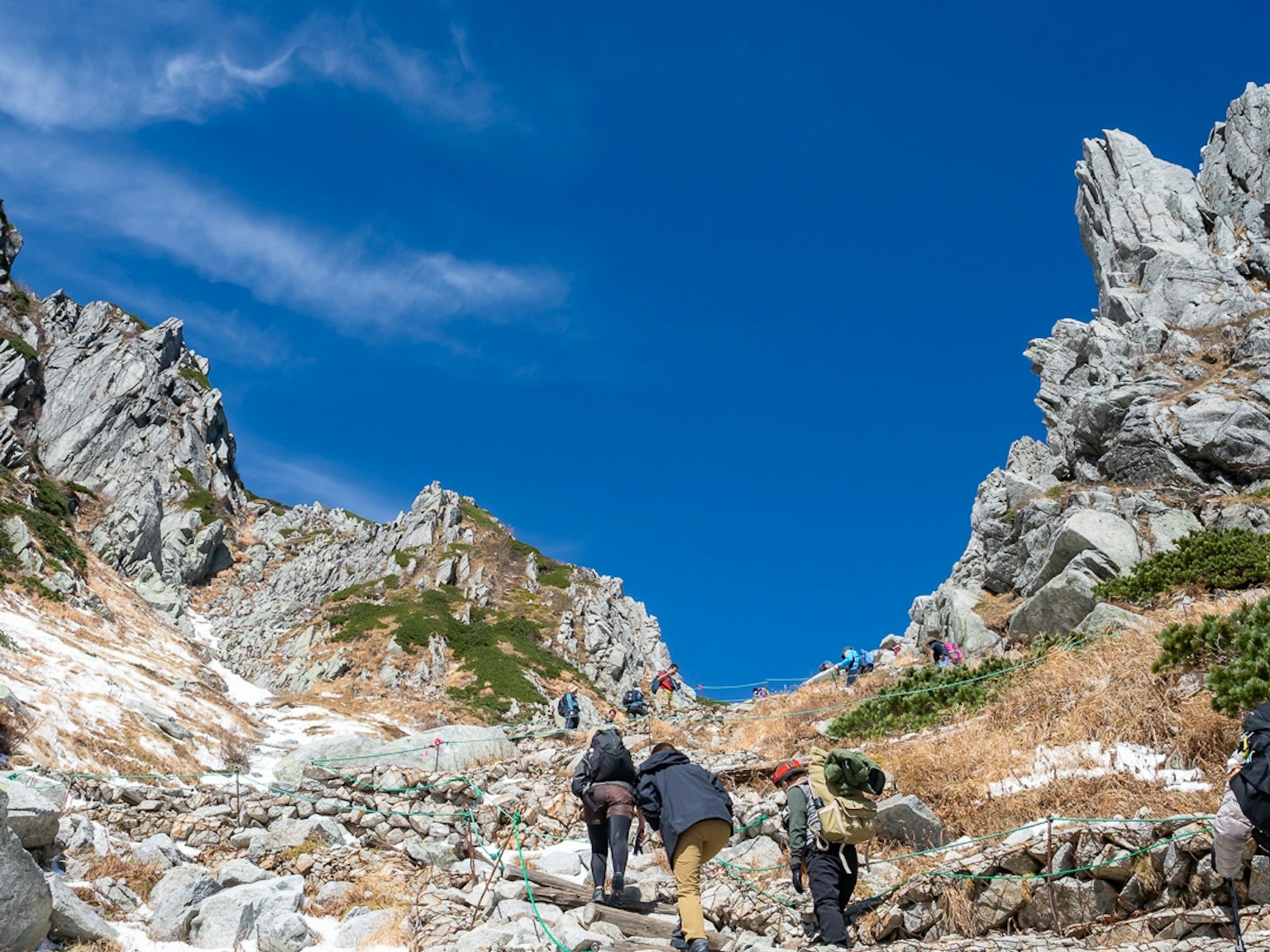 Hikers ascending a rocky trail under a clear blue sky