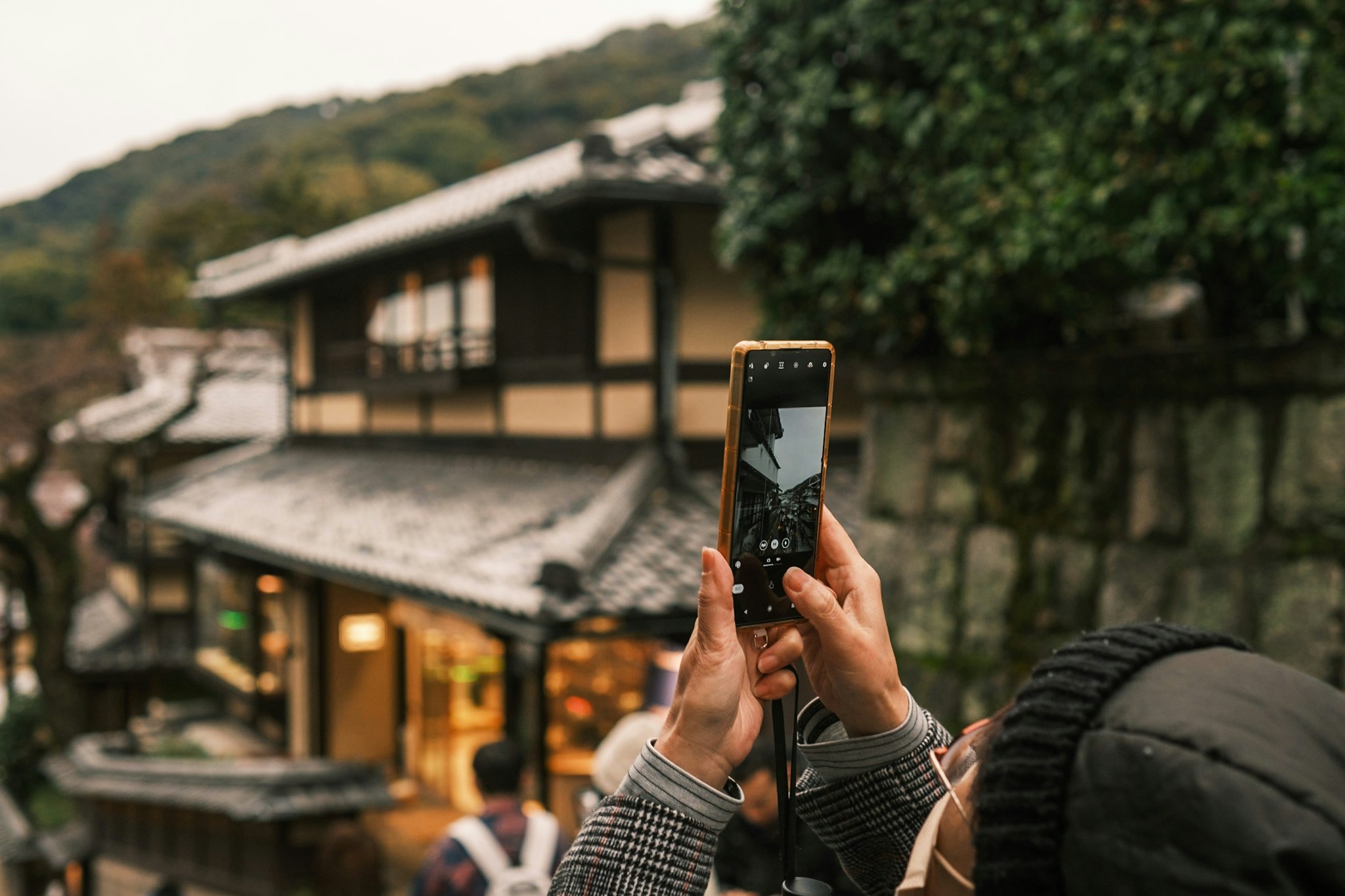 hands holding a smartphone photographing a traditional-style village street