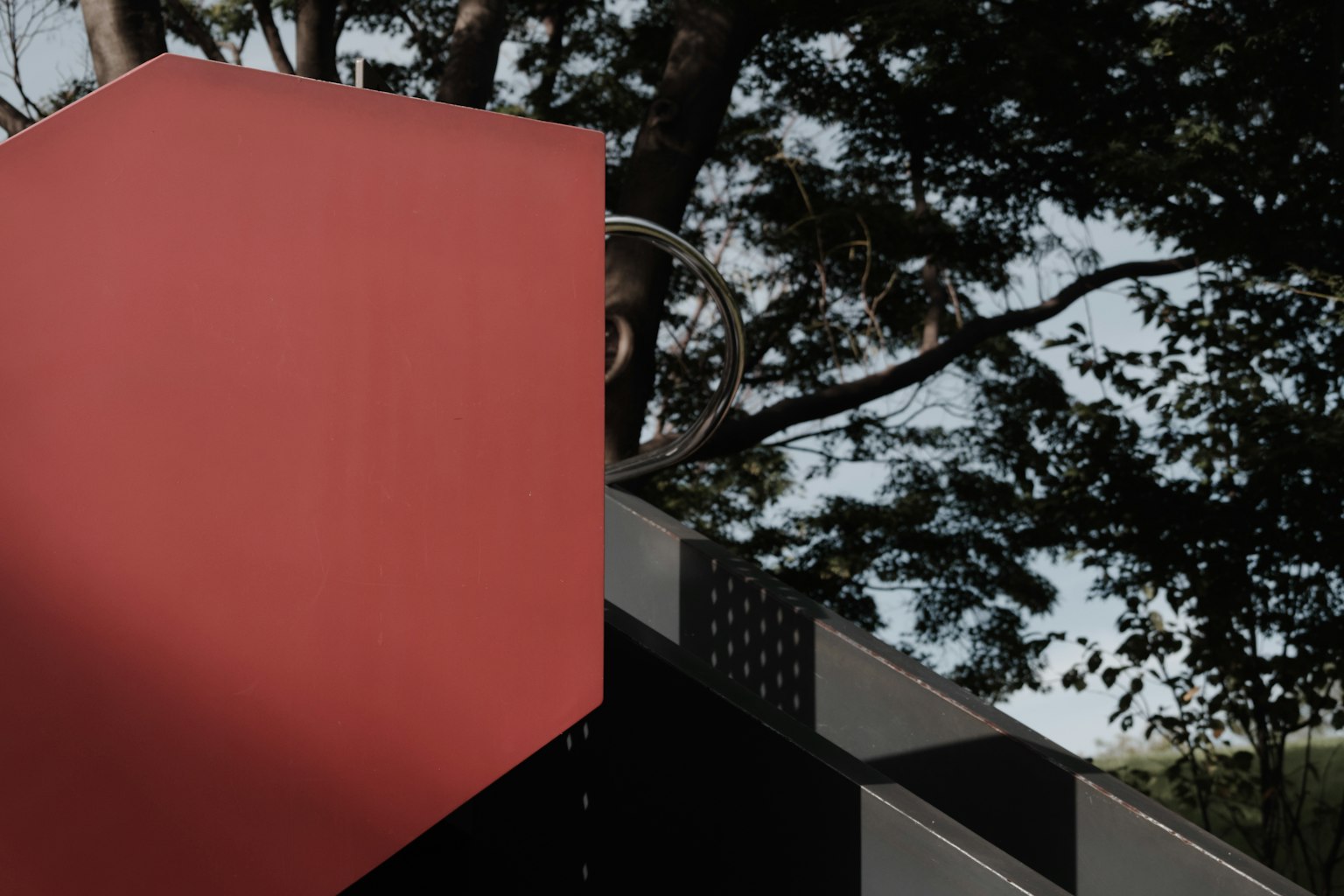 Image featuring a red cubic structure against a backdrop of green trees