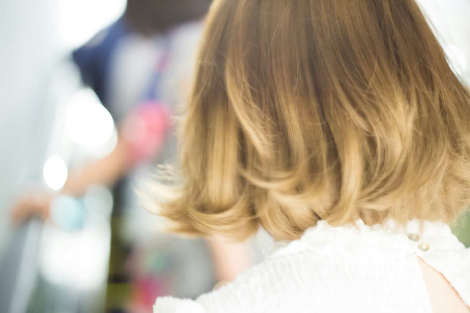 Primer plano del cabello rubio de una mujer desde atrás con una figura borrosa al fondo