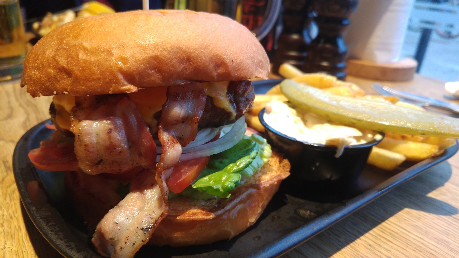 Burger lezat dengan bacon selada tomat dan kentang goreng di atas meja kayu
