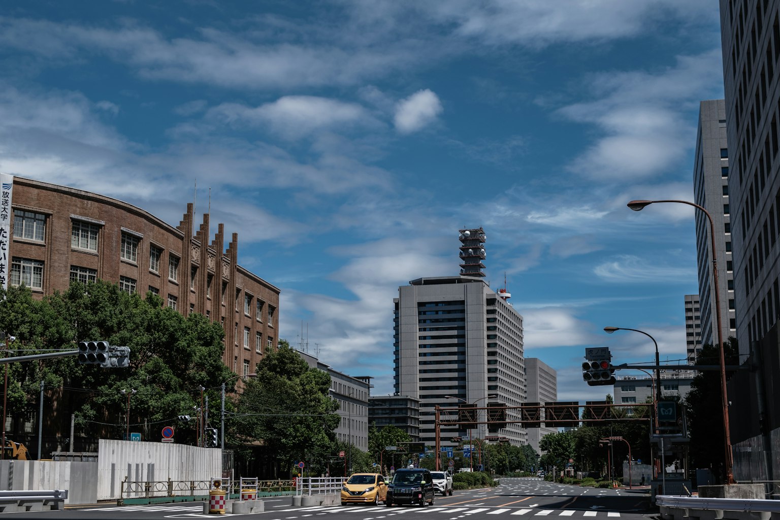 Pemandangan kota di bawah langit biru dengan awan menampilkan bangunan tua dan modern di sepanjang jalan