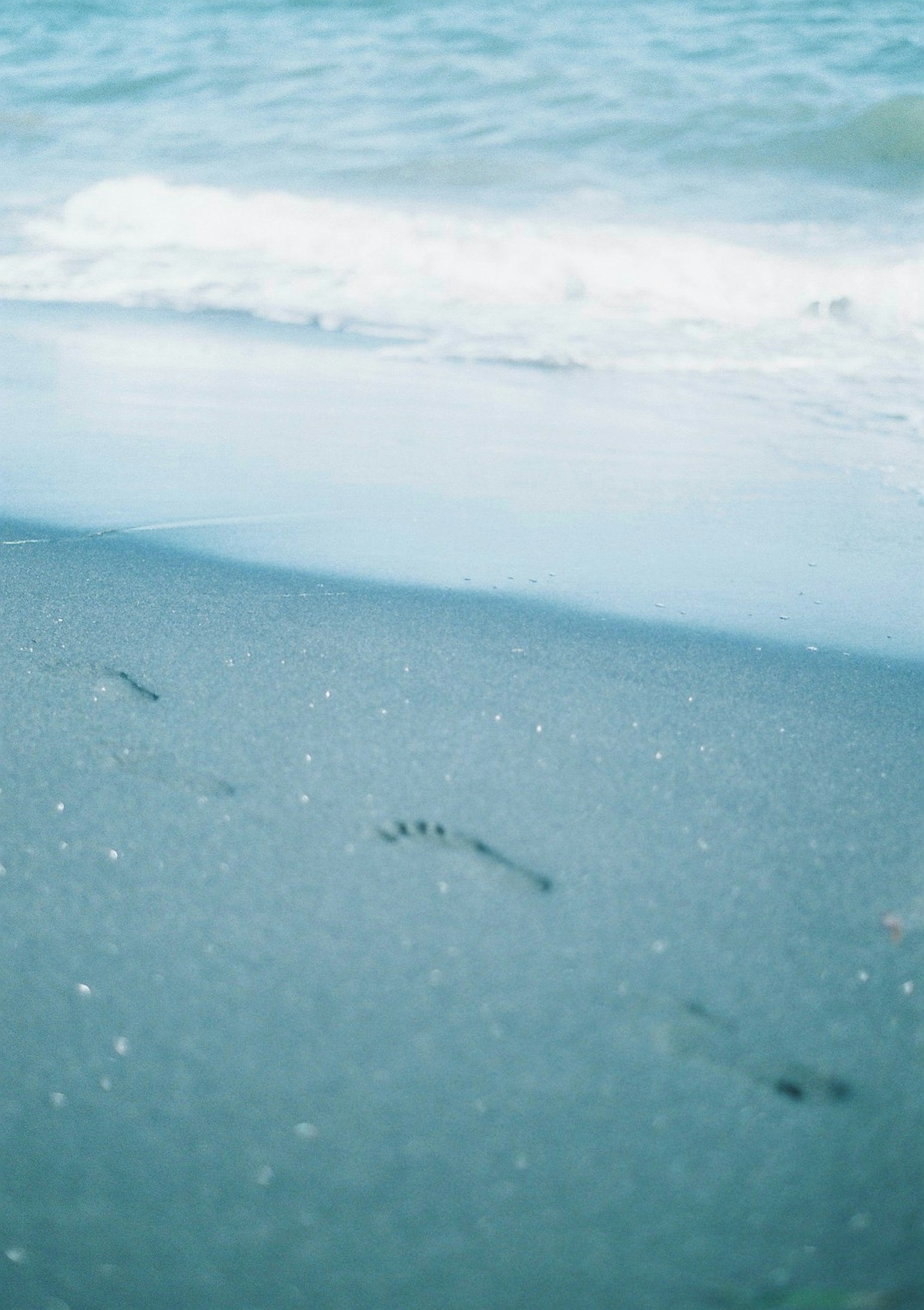 Jejak kaki di pantai berpasir dengan ombak biru