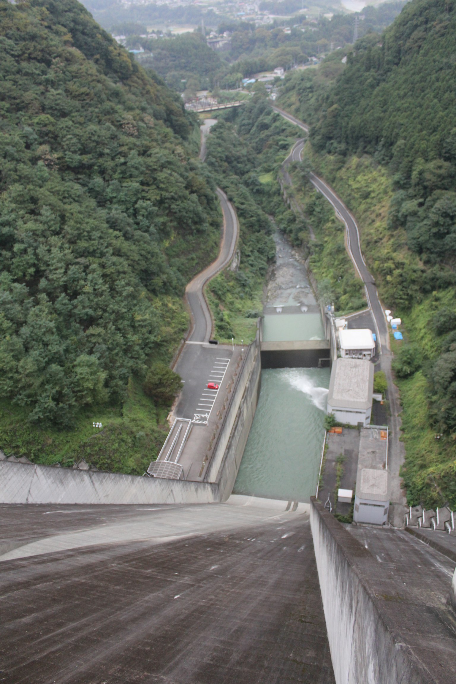 Vista aerea da un alto dam mostrando montagne verdeggianti e un canale d'acqua