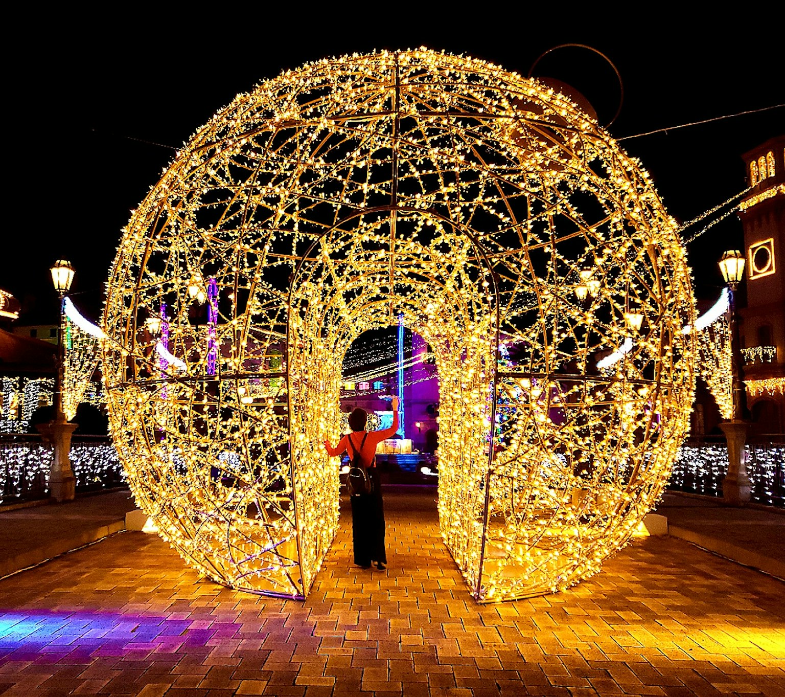 Una persona in piedi davanti a un grande arco sferico decorato con luci di notte