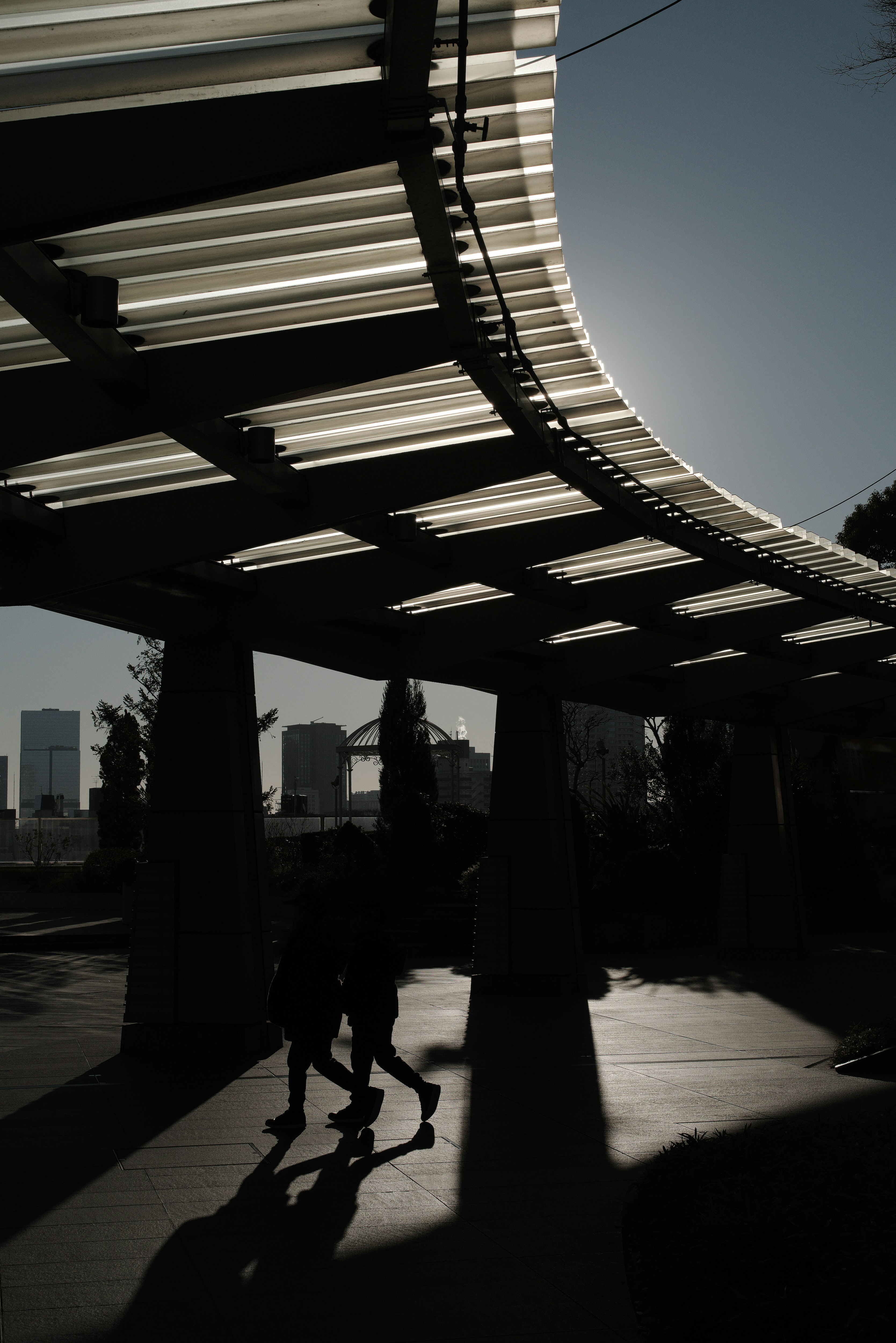 two people walking silhouettes along a covered walkway with shadows in a cityscape