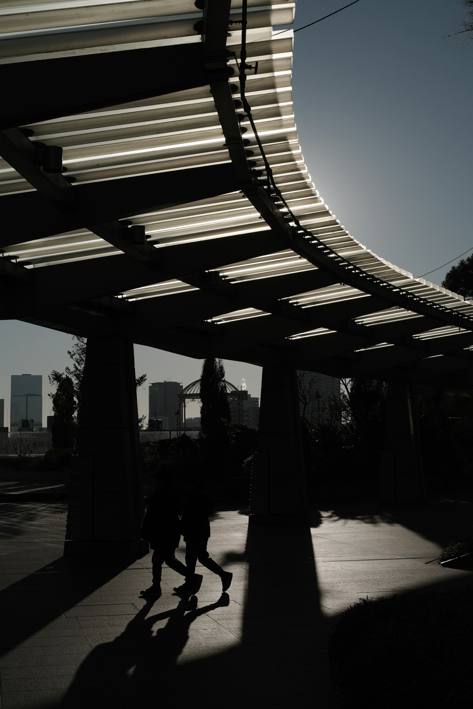 Sillhouette di persone che camminano sotto un tetto curvo con sfondo urbano e forte contrasto