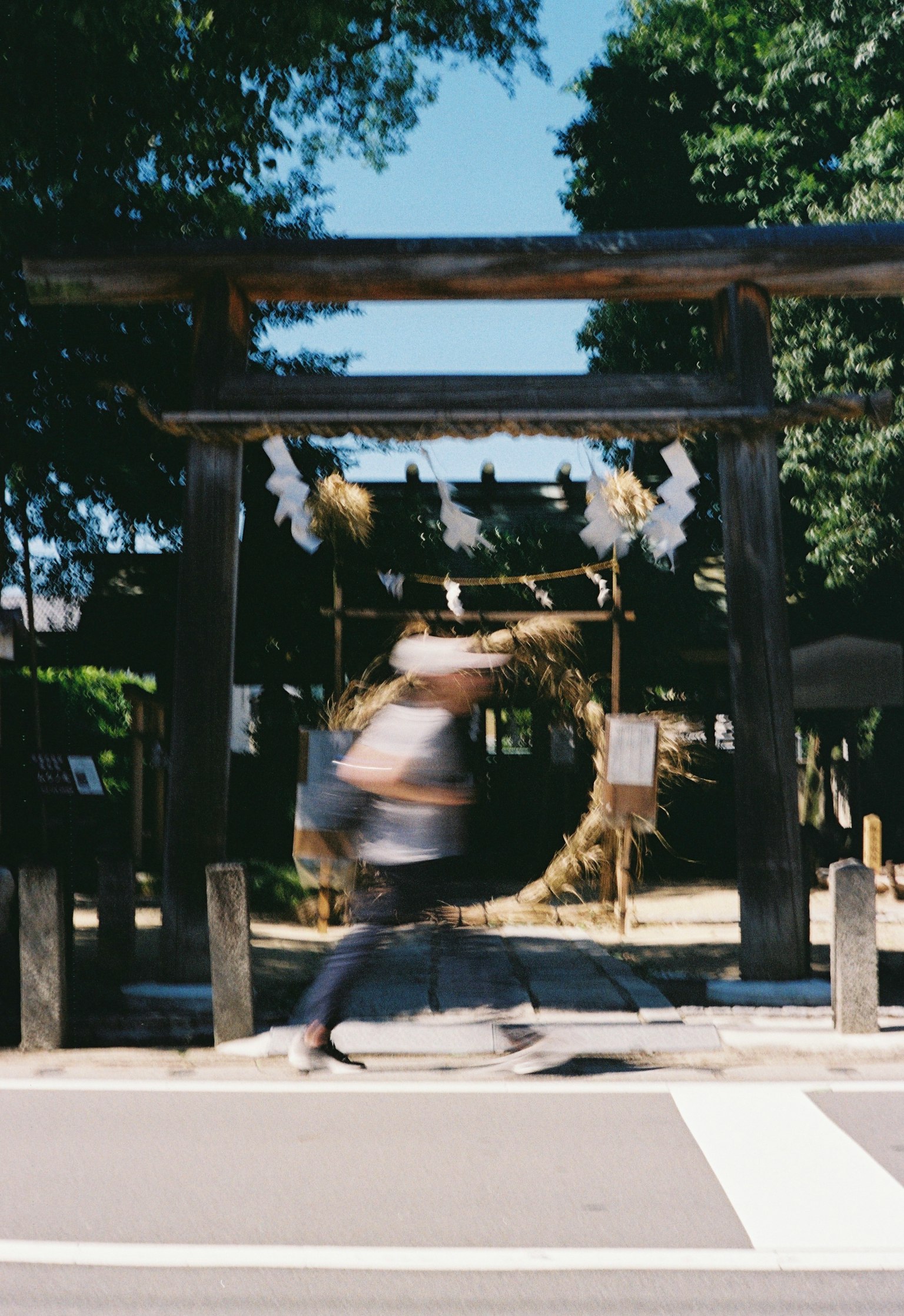 A blurred figure running past a shrine gate adorned with decorative wreaths