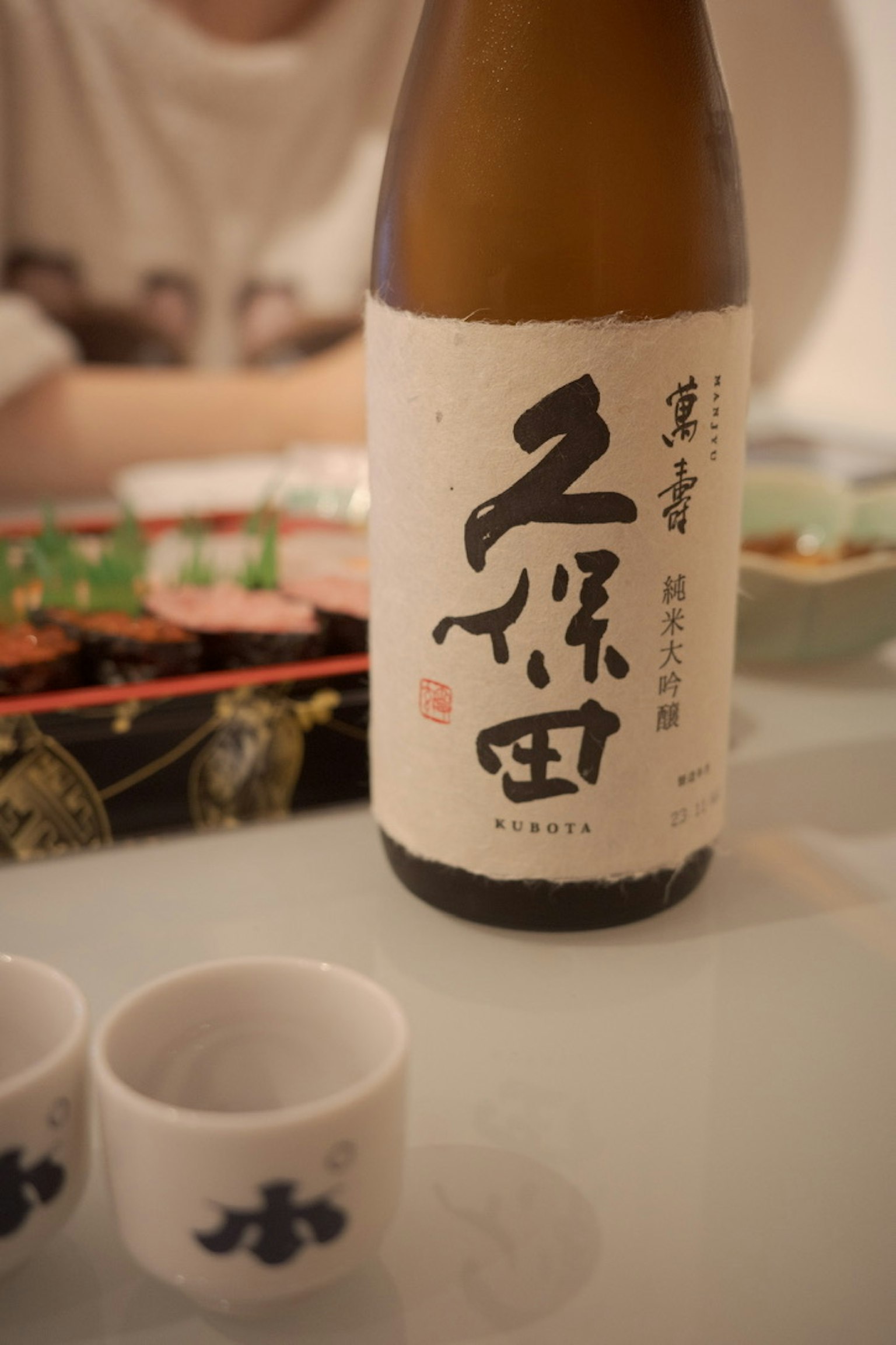 Une bouteille de saké avec des petites coupes à saké sur une table
