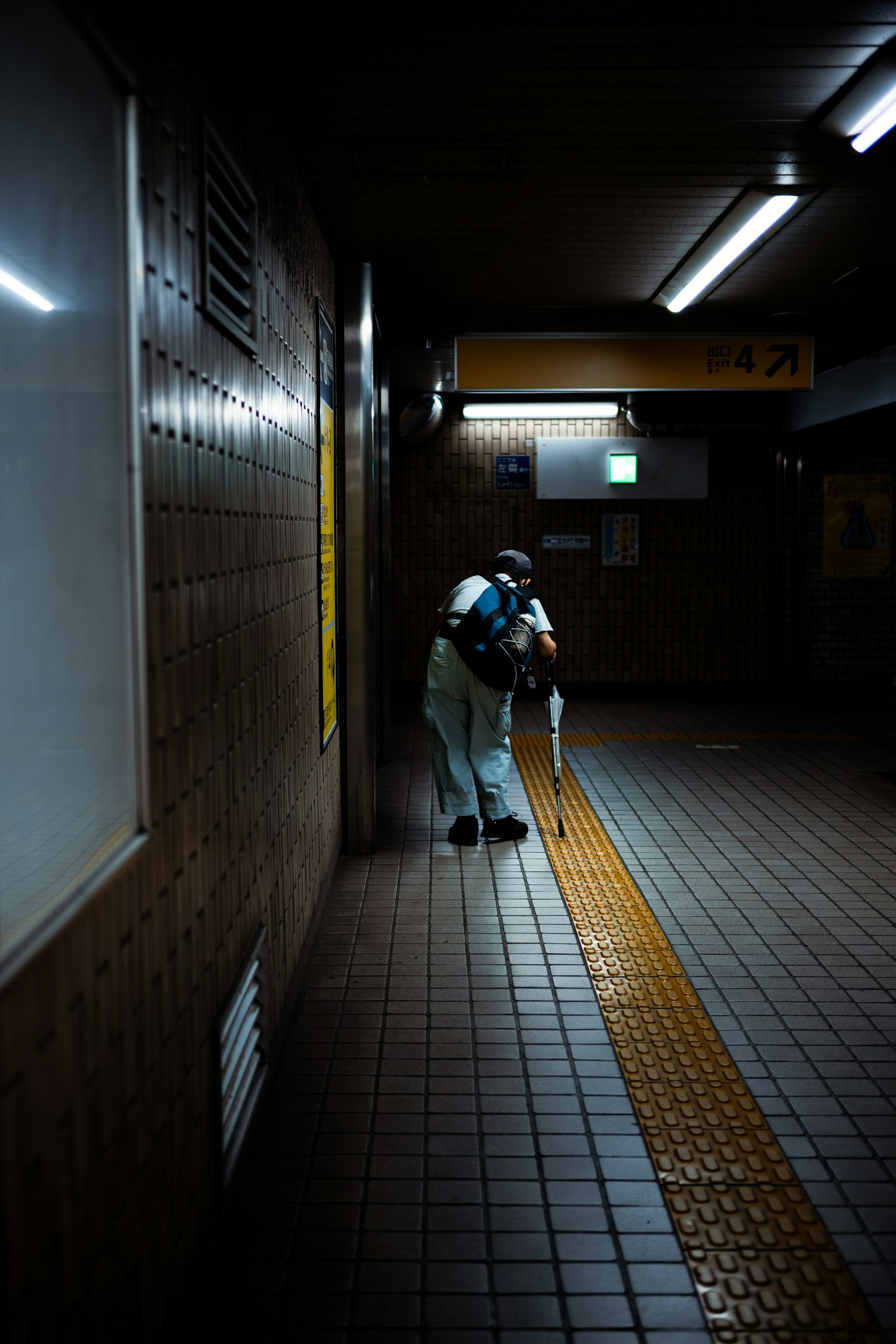 Una persona agachada en un pasillo de metro débilmente iluminado sosteniendo un paraguas