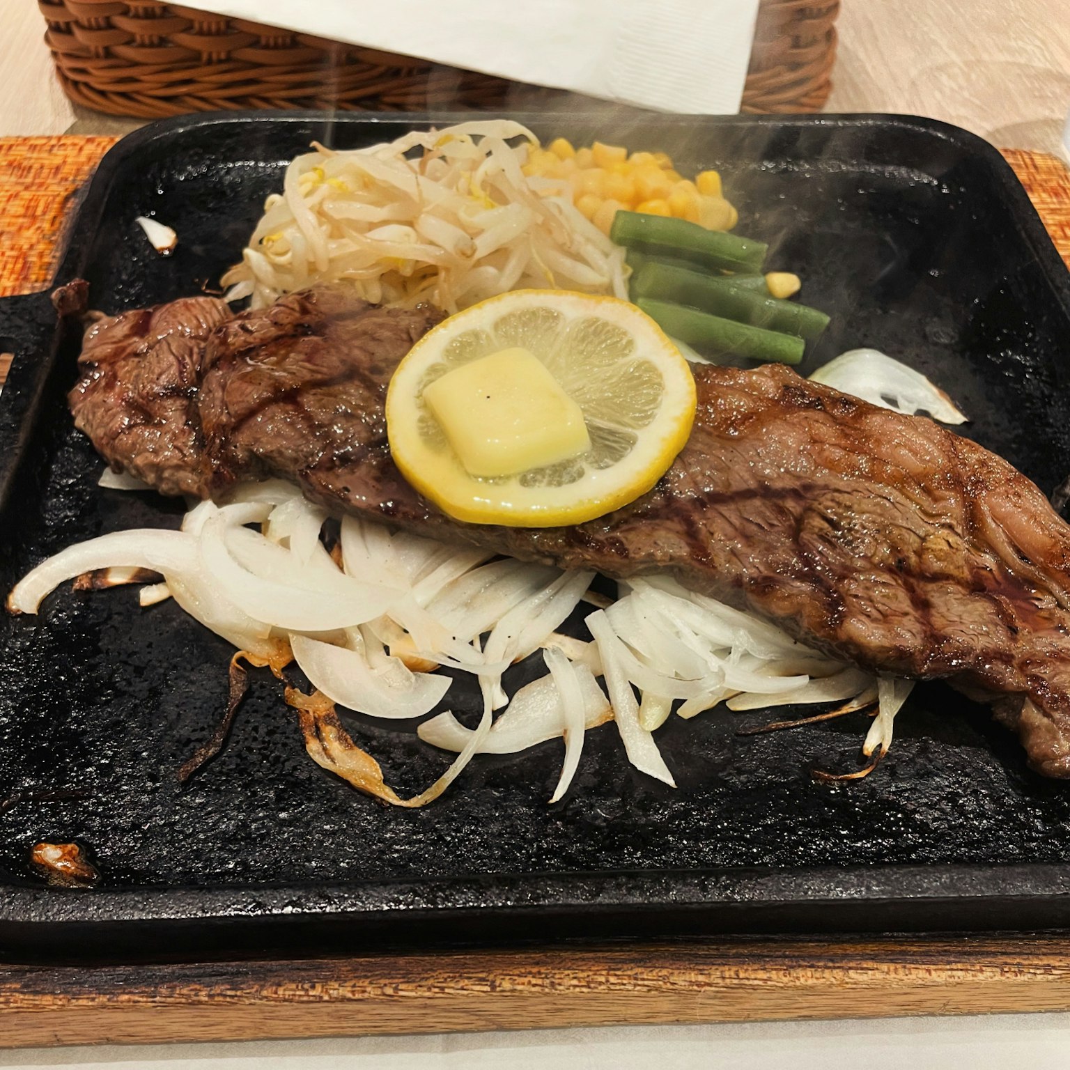 Bistecca sfrigolante su un piatto caldo guarnita con limone e burro accanto a verdure