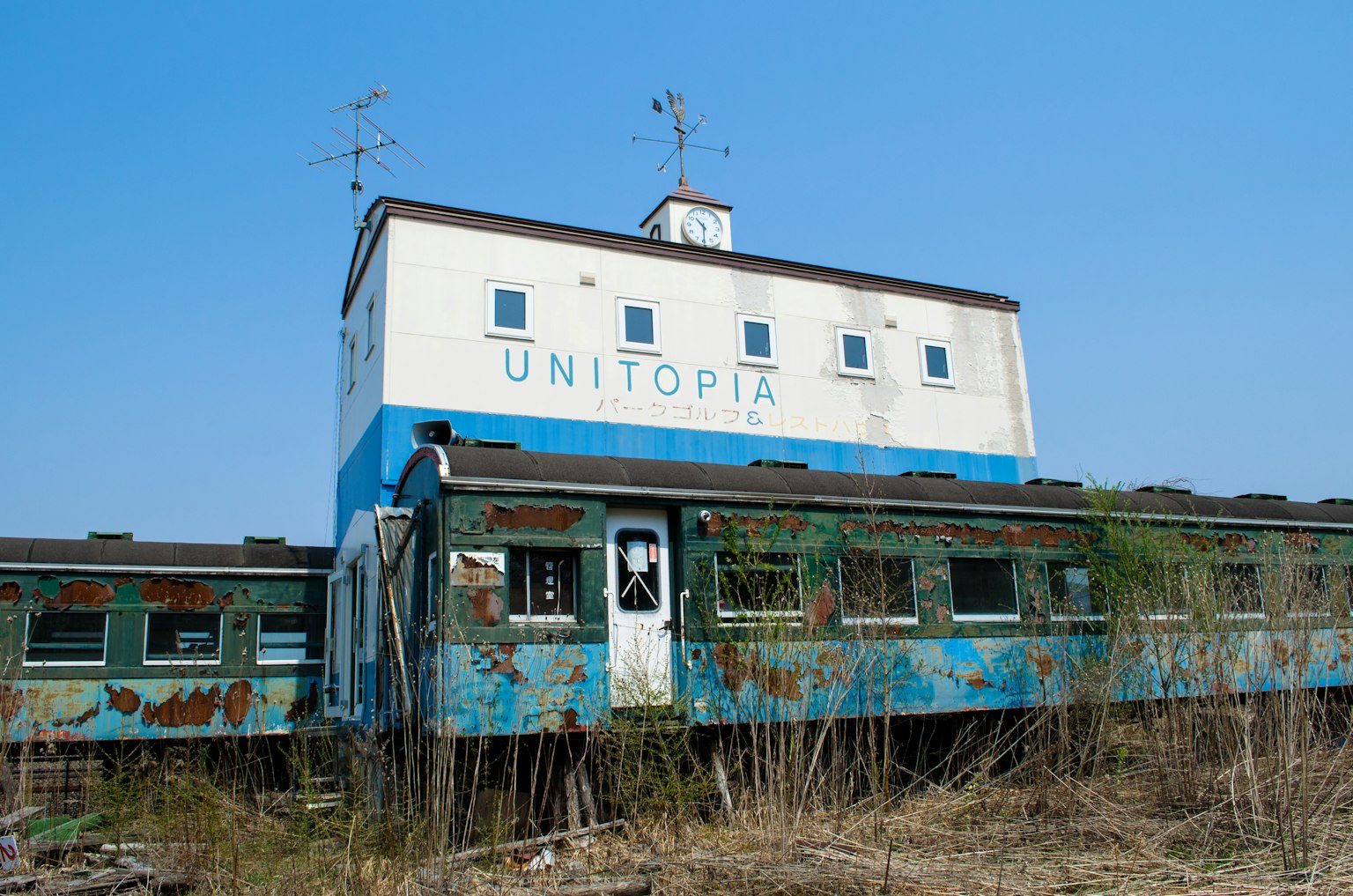 Wagon de train abandonné et bâtiment avec enseigne 'UNITOPIA' sous un ciel bleu
