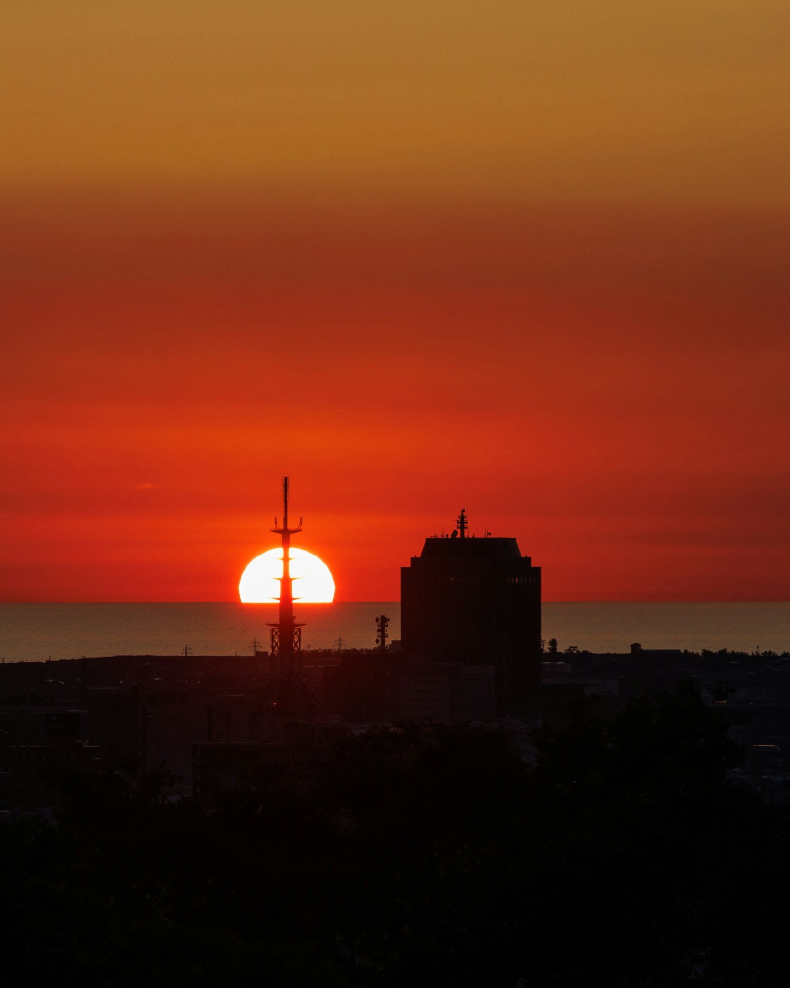 Silhouette de bâtiments et d'une tour de communication contre un soleil couchant