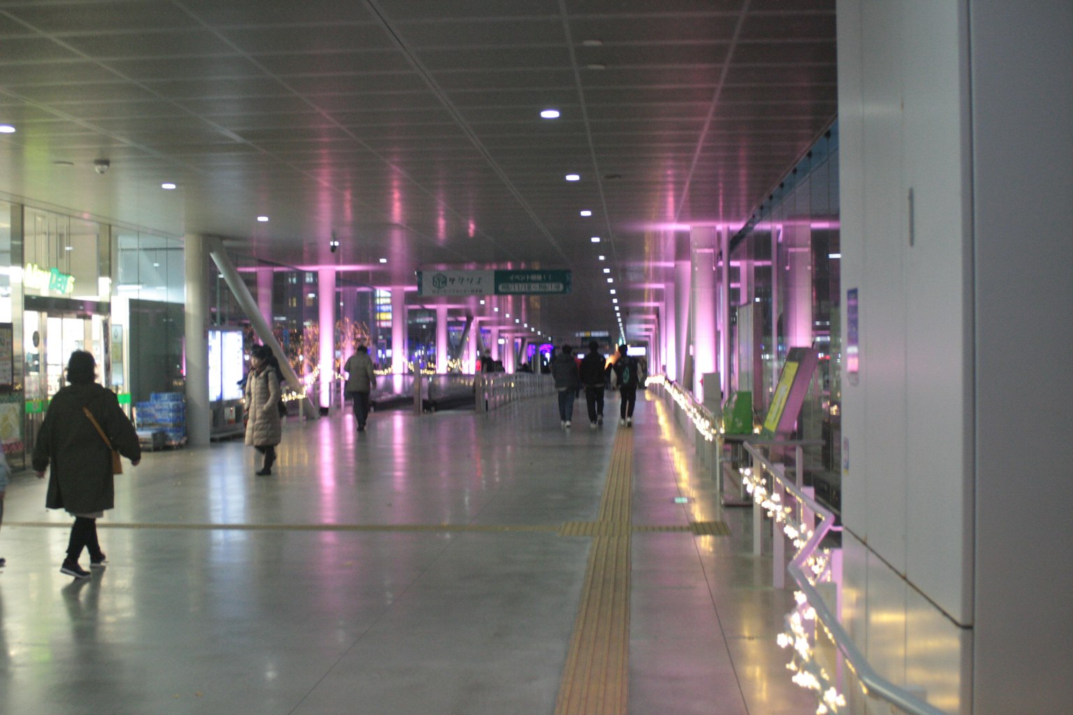Amplio pasillo iluminado con luces rosas brillantes con personas caminando