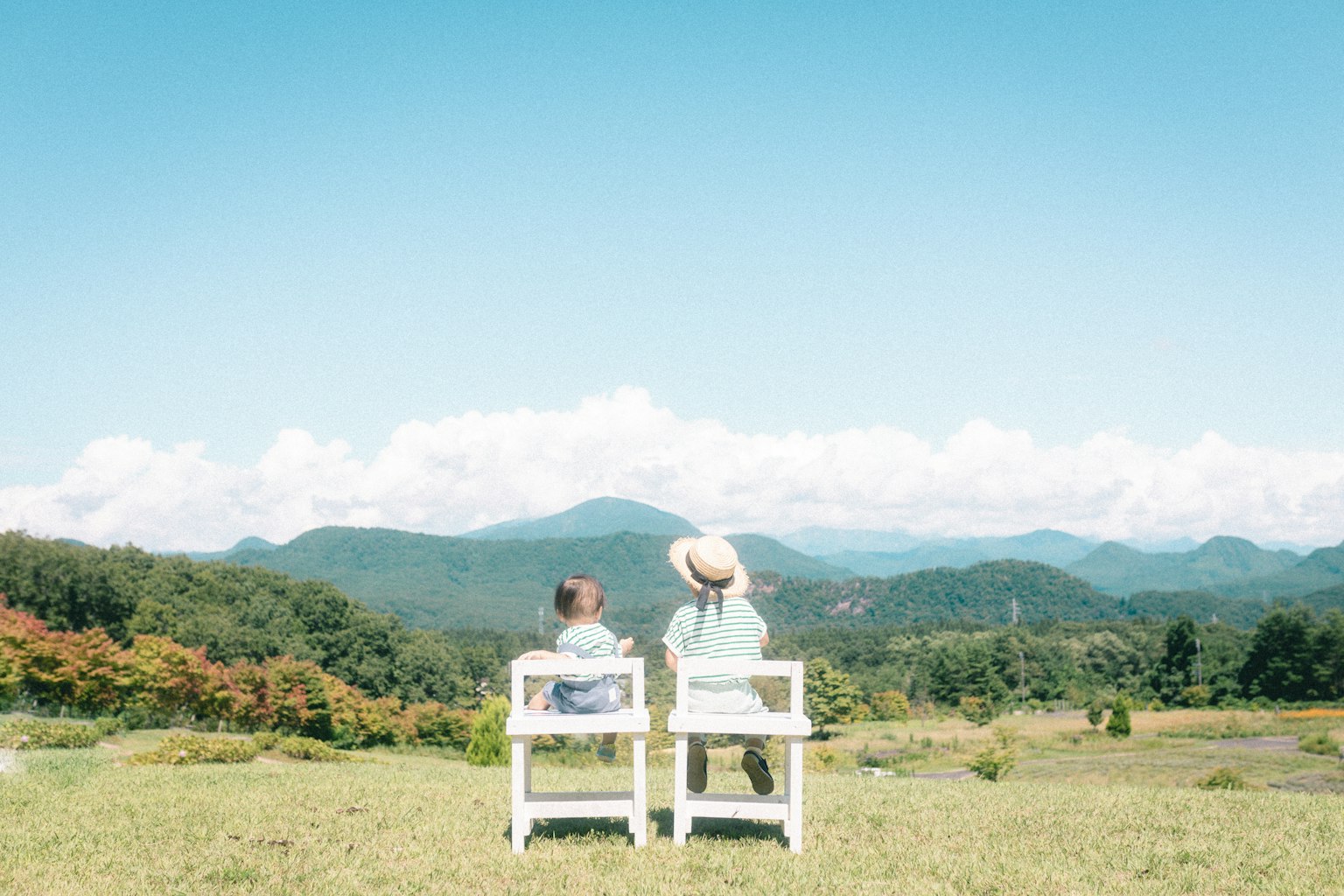 二人の人が白い椅子に座り、山々を見つめている風景