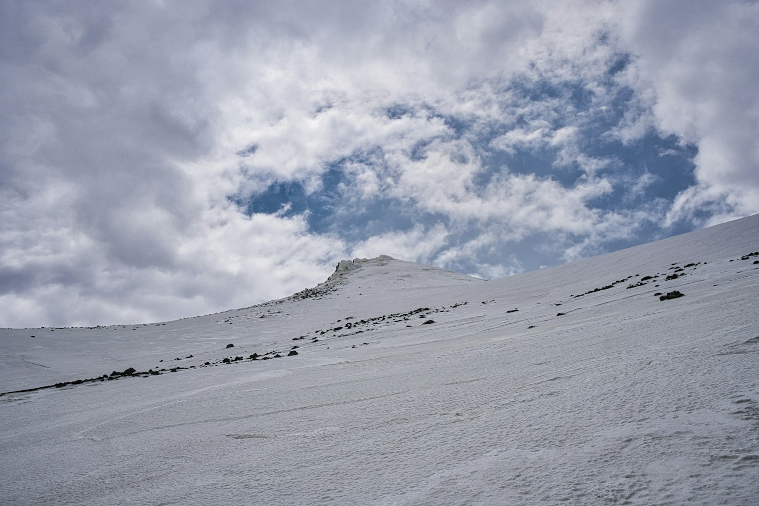 Pendio di montagna coperto di neve con cielo blu e nuvole