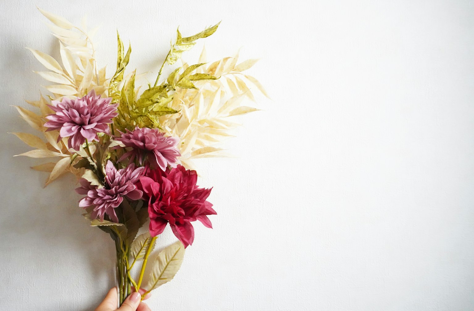Un bouquet de fleurs et de feuilles tenu à la main sur un fond simple