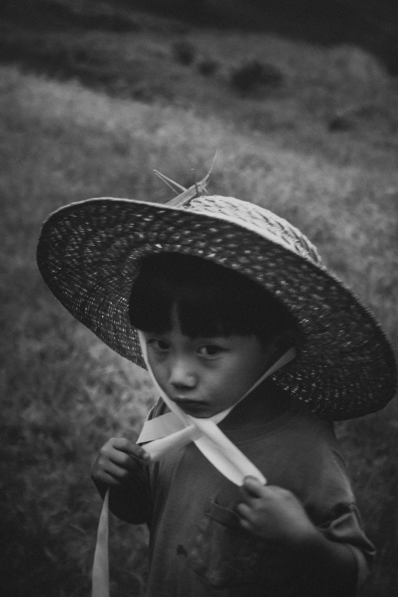黒白の写真で麦わら帽子をかぶった子供が立っている