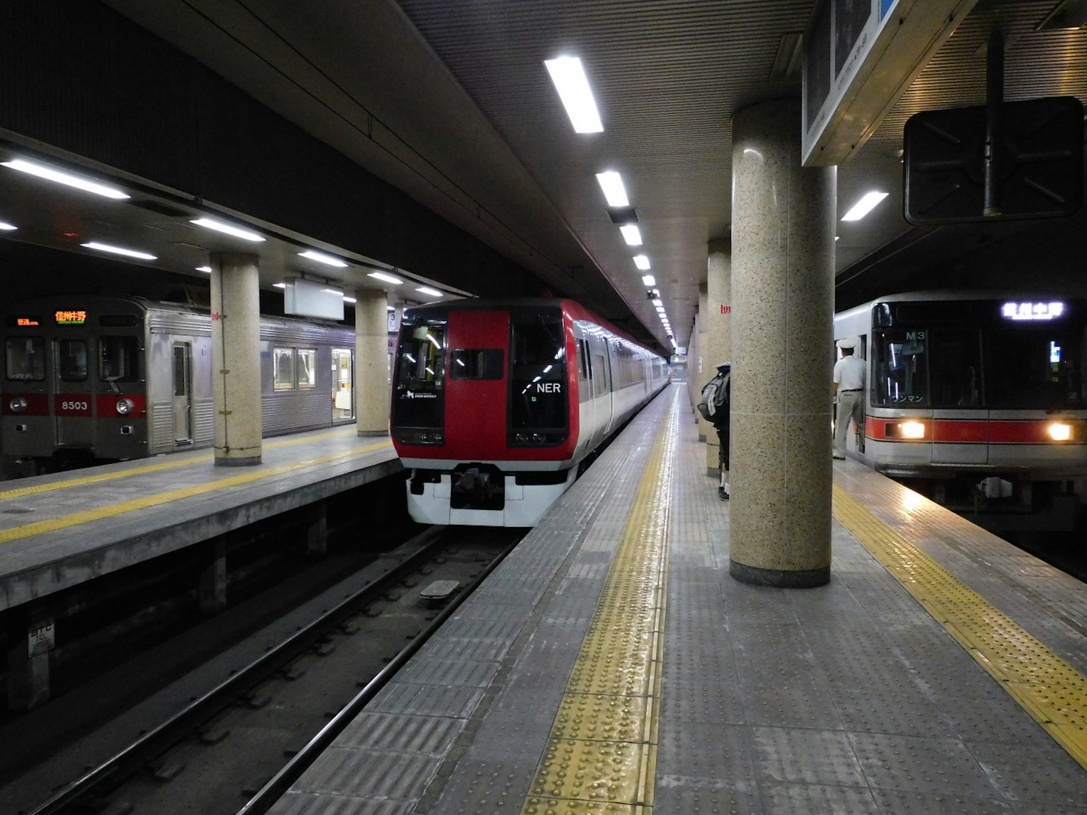 Vue d'une station de métro avec un train rouge et un train noir sur le quai
