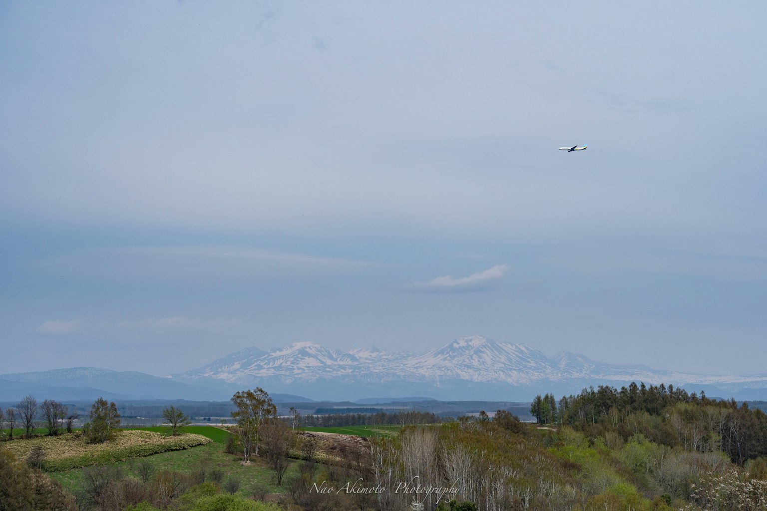 Landscape with green hills and snow-capped mountains under a blue sky