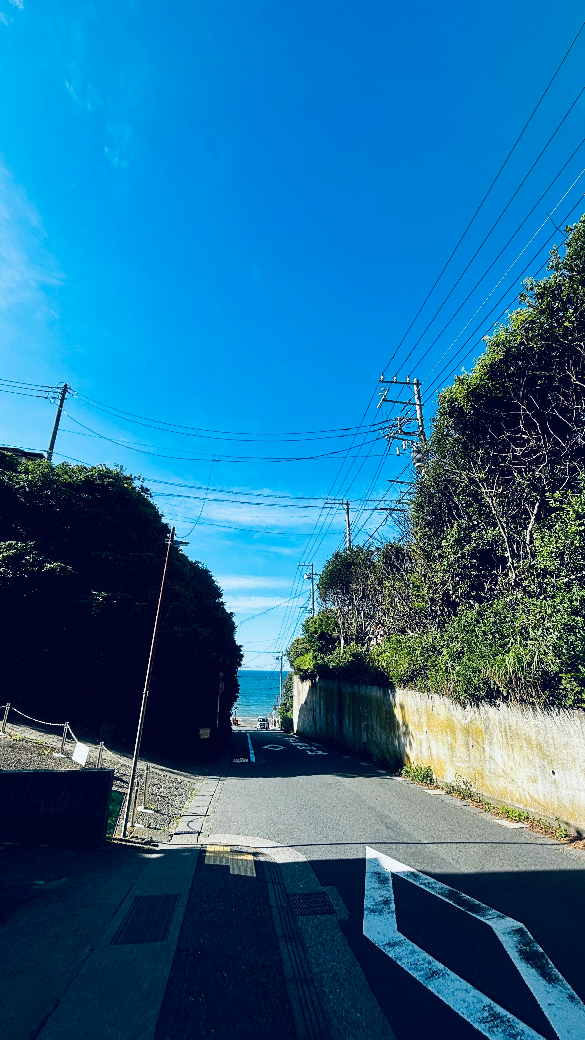 青空の下の坂道と電線が走る道