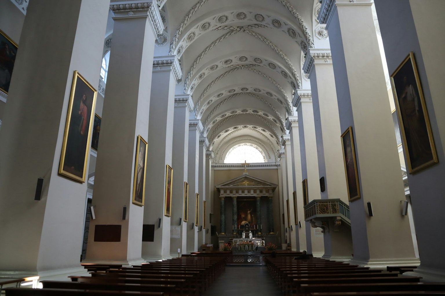 Amplio interior de una iglesia con pinturas en las paredes bancos largos que conducen al altar
