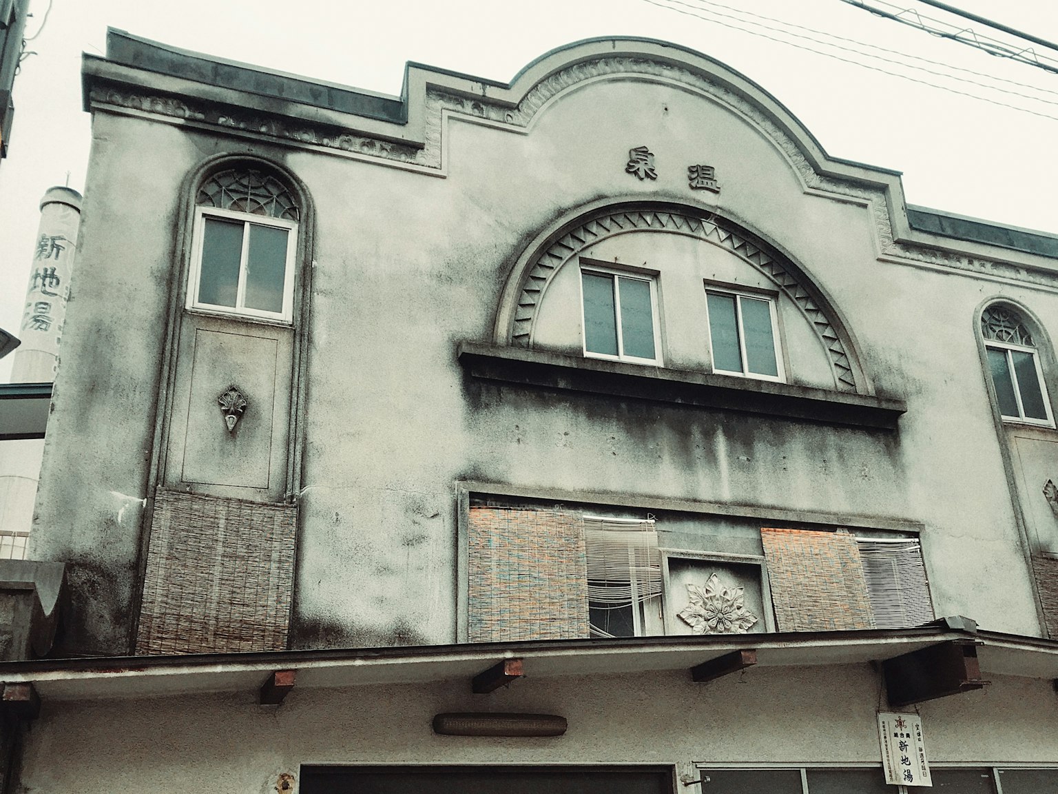 Façade d'un vieux bâtiment avec fenêtres, murs gris usés, caractéristiques d'arc décoratif