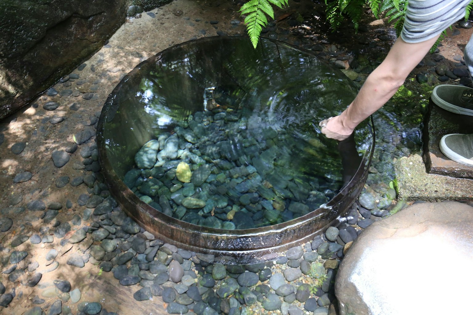 Một bàn tay chạm vào nước trong bể tròn đầy đá màu sắc