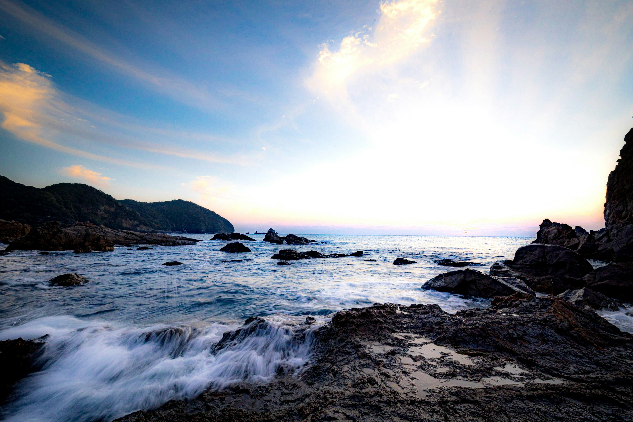 pantai berbatu saat senja dengan ombak menghantam