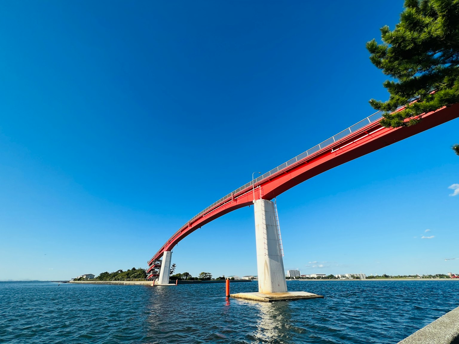 Jembatan merah melengkung di atas air di bawah langit biru yang cerah