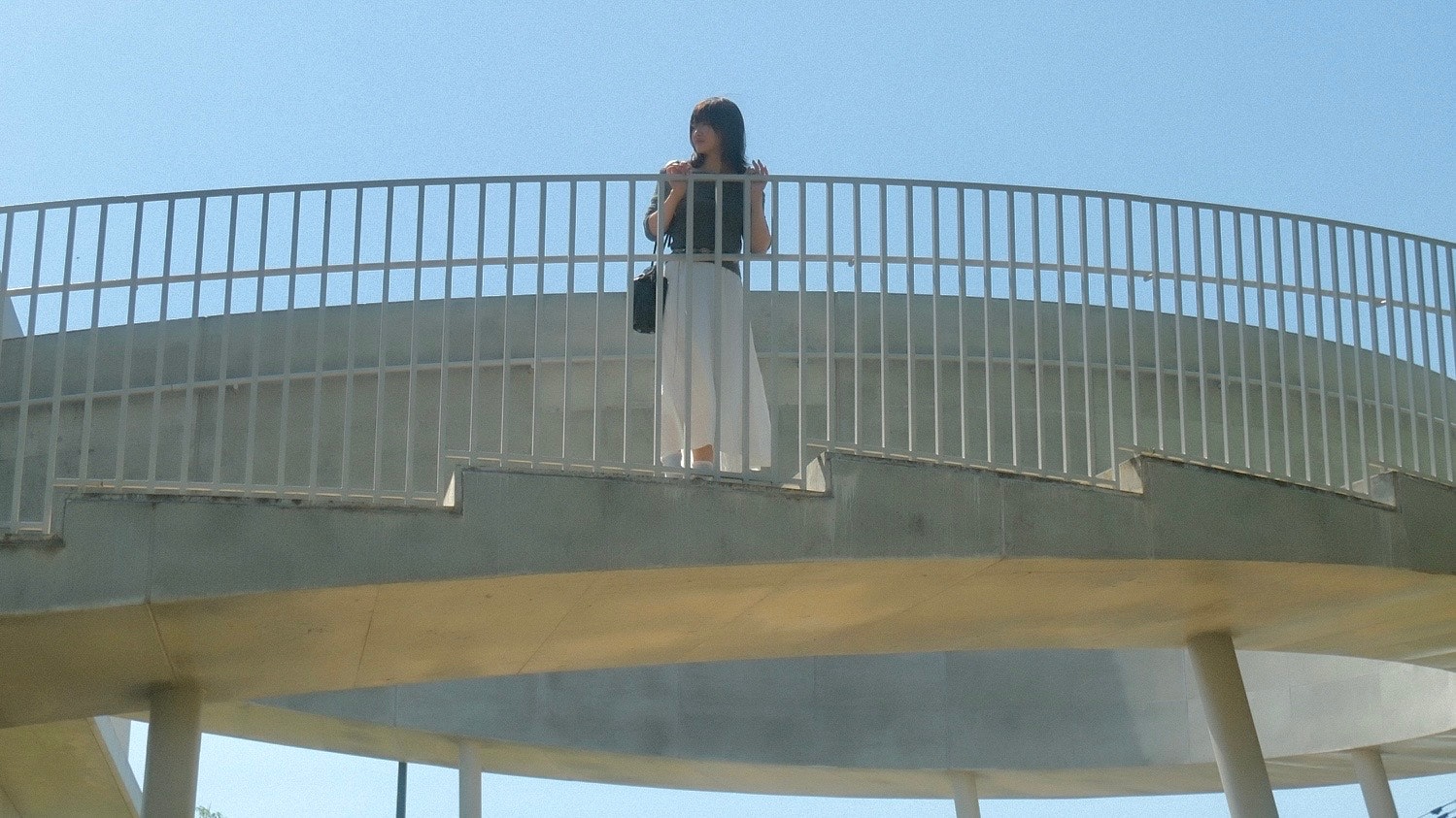 藍天之下，橋上拿著手機的女性