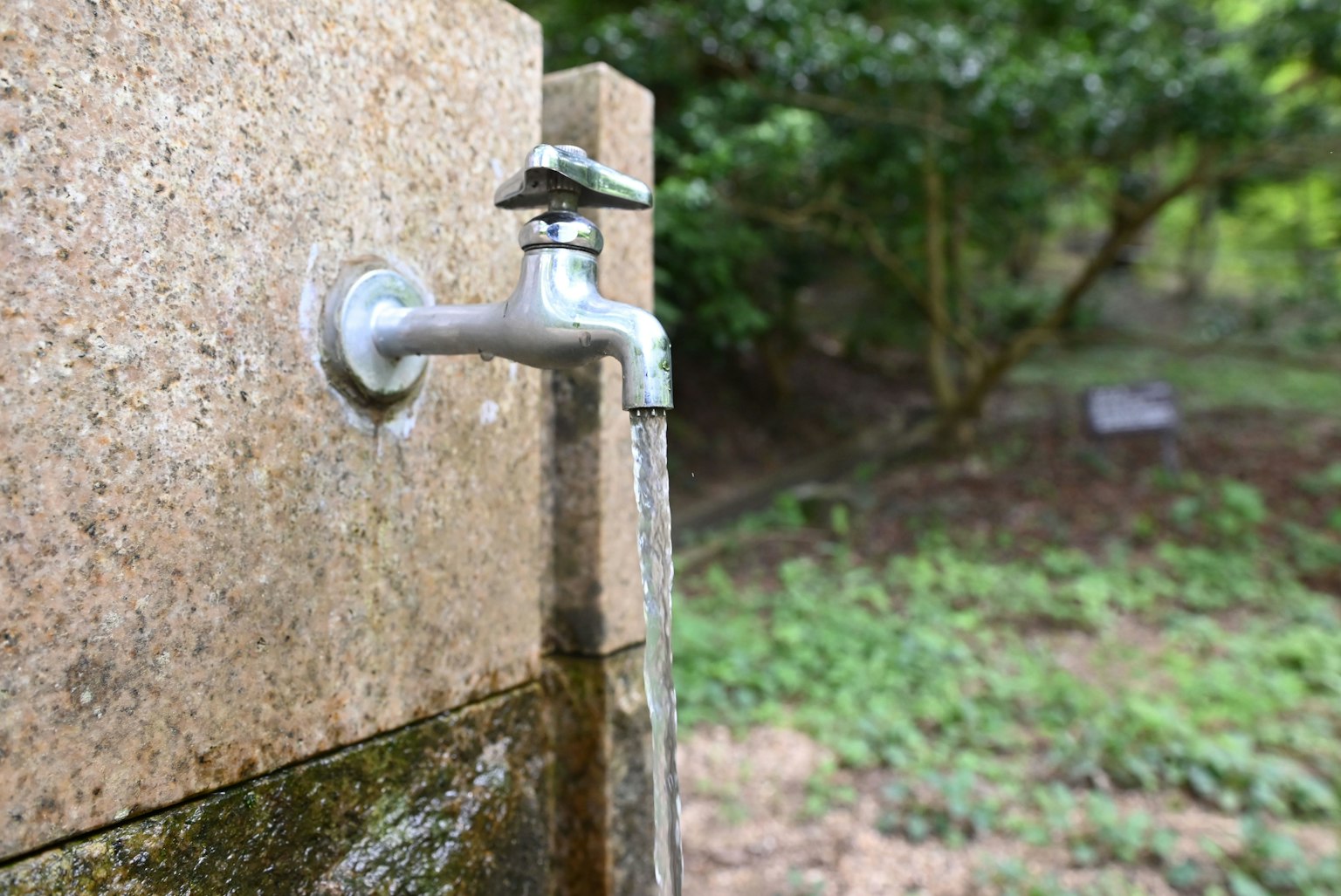 Rubinetto che versa acqua da un muro di pietra in un paesaggio verde
