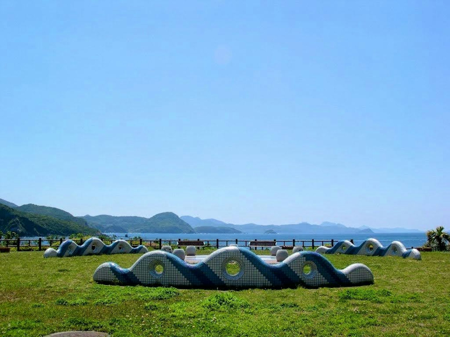 Escultura de piedra en forma de ola bajo un cielo azul con vista al océano