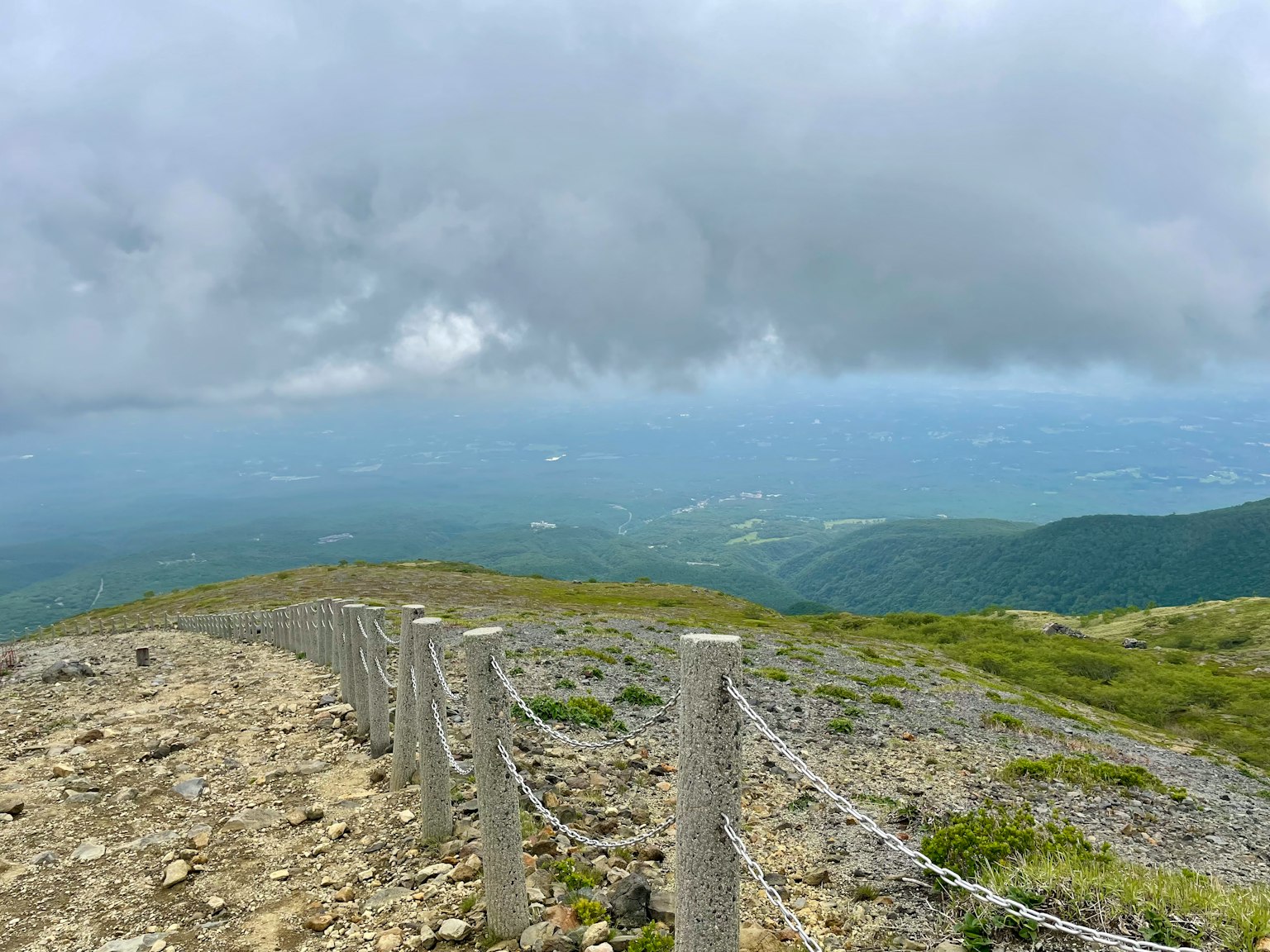 Une vue panoramique depuis un sommet de montagne avec un ciel nuageux et un chemin rocailleux bordé d'une clôture
