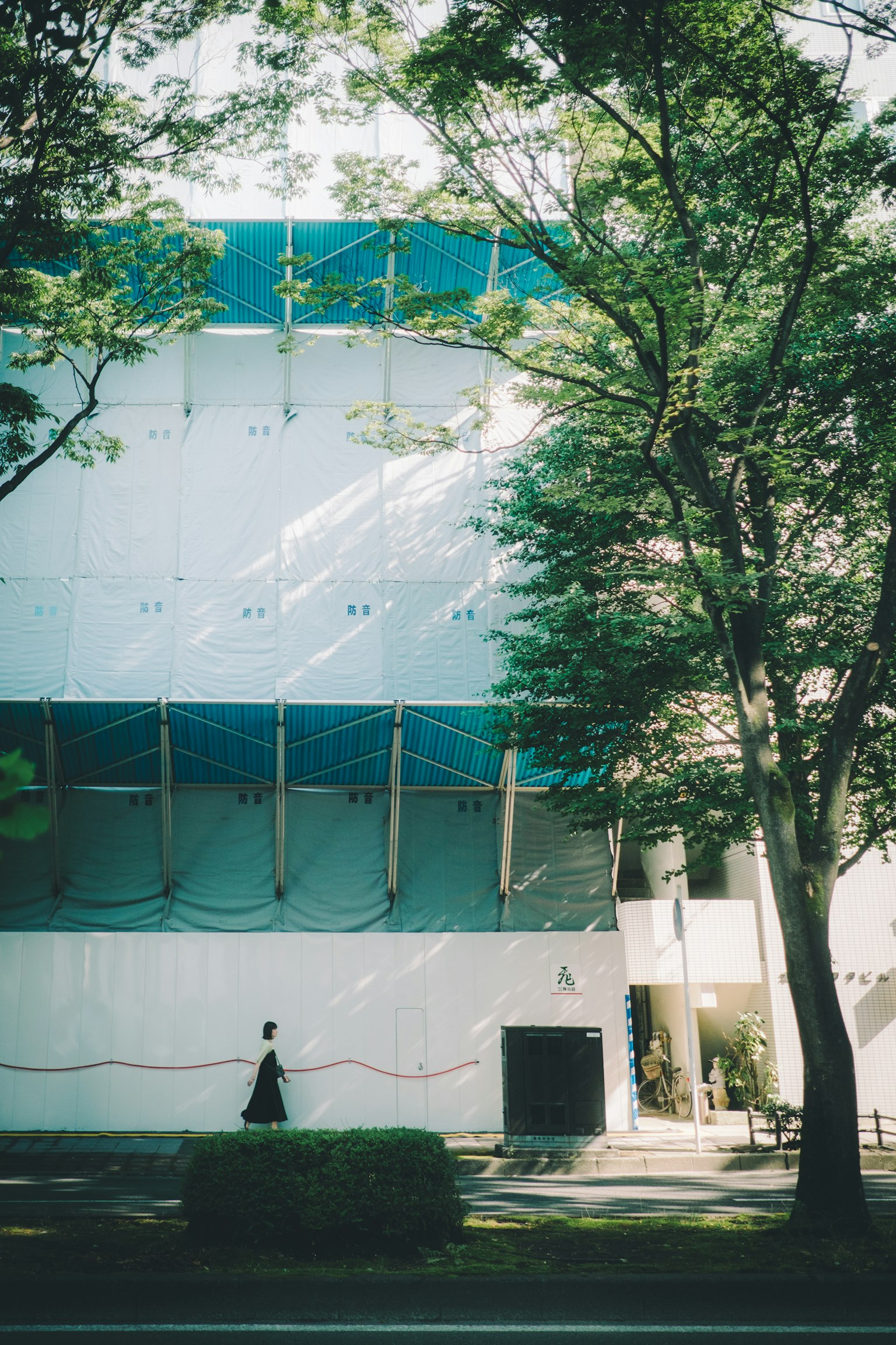 A woman walking in front of a building with a blue roof and green trees